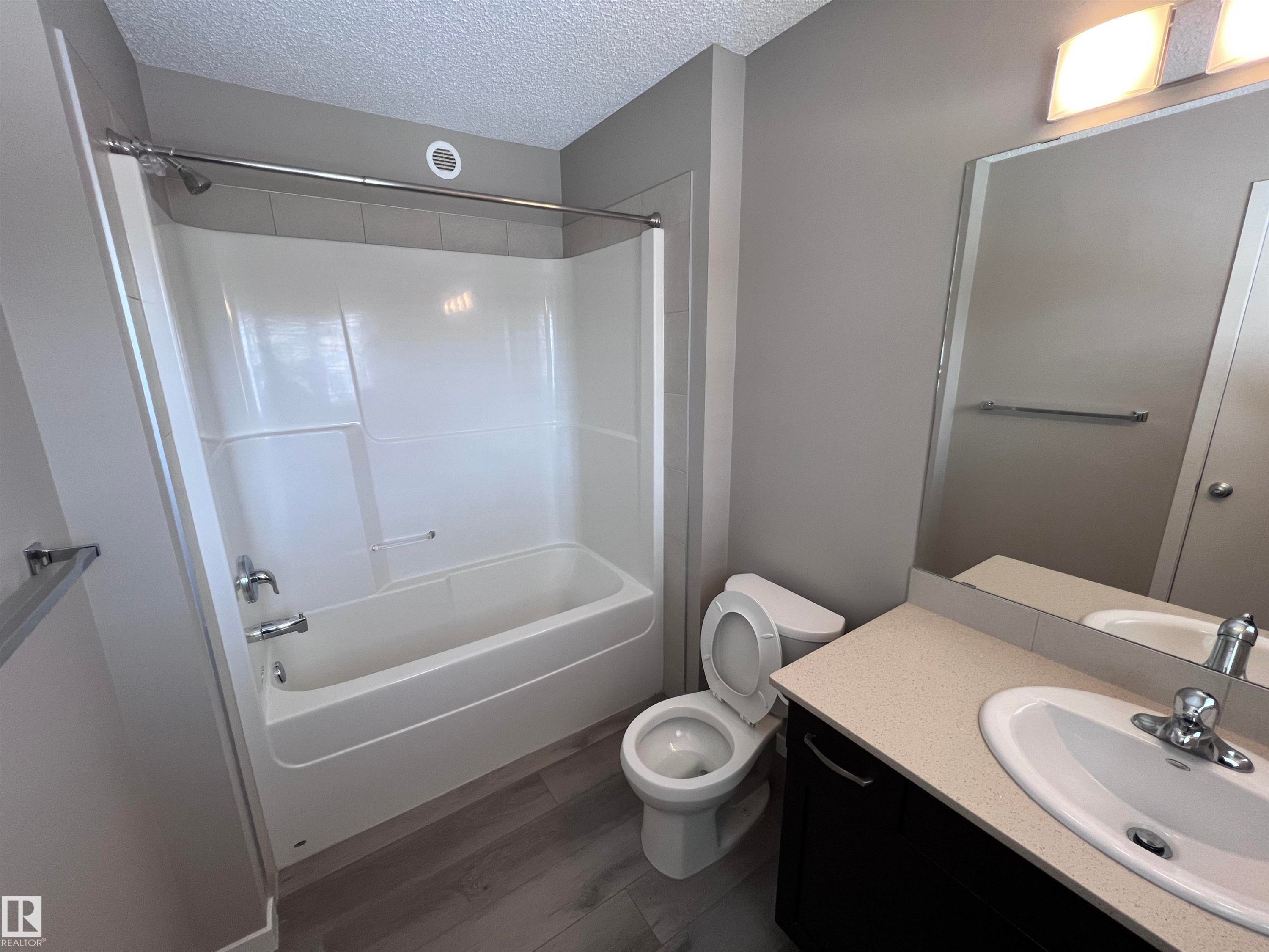 Bathroom featuring a bathtub with an integrated shower, a vanity with a light-colored countertop, and a large mirror - 1421 26 Avenue, Edmonton, AB - Indoor Photo Showing Bathroom