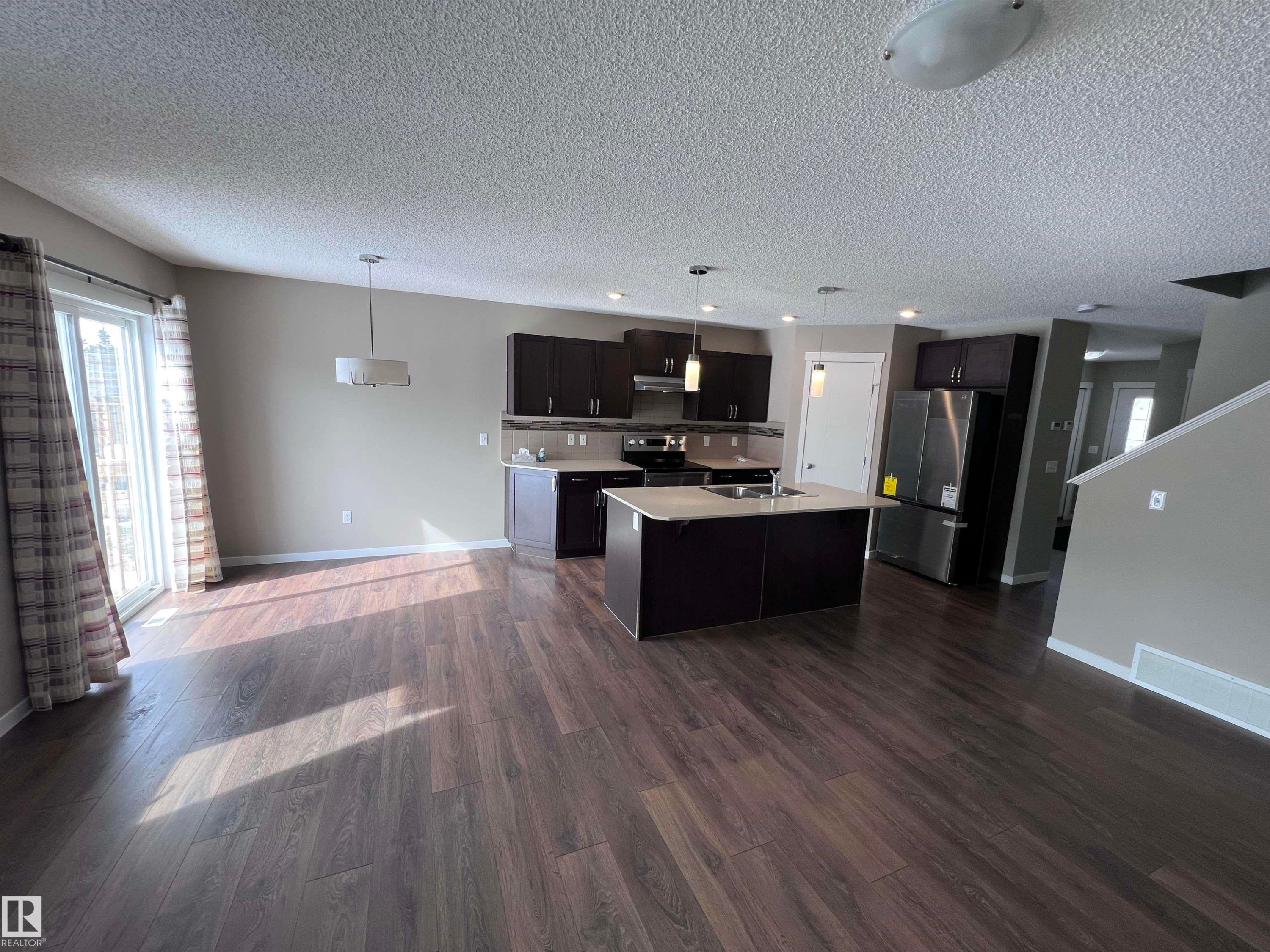 Spacious open concept living area featuring dark wood flooring, a kitchen island with a sink, and a patio door providing natural light - 1421 26 Avenue, Edmonton, AB - Indoor Photo Showing Kitchen