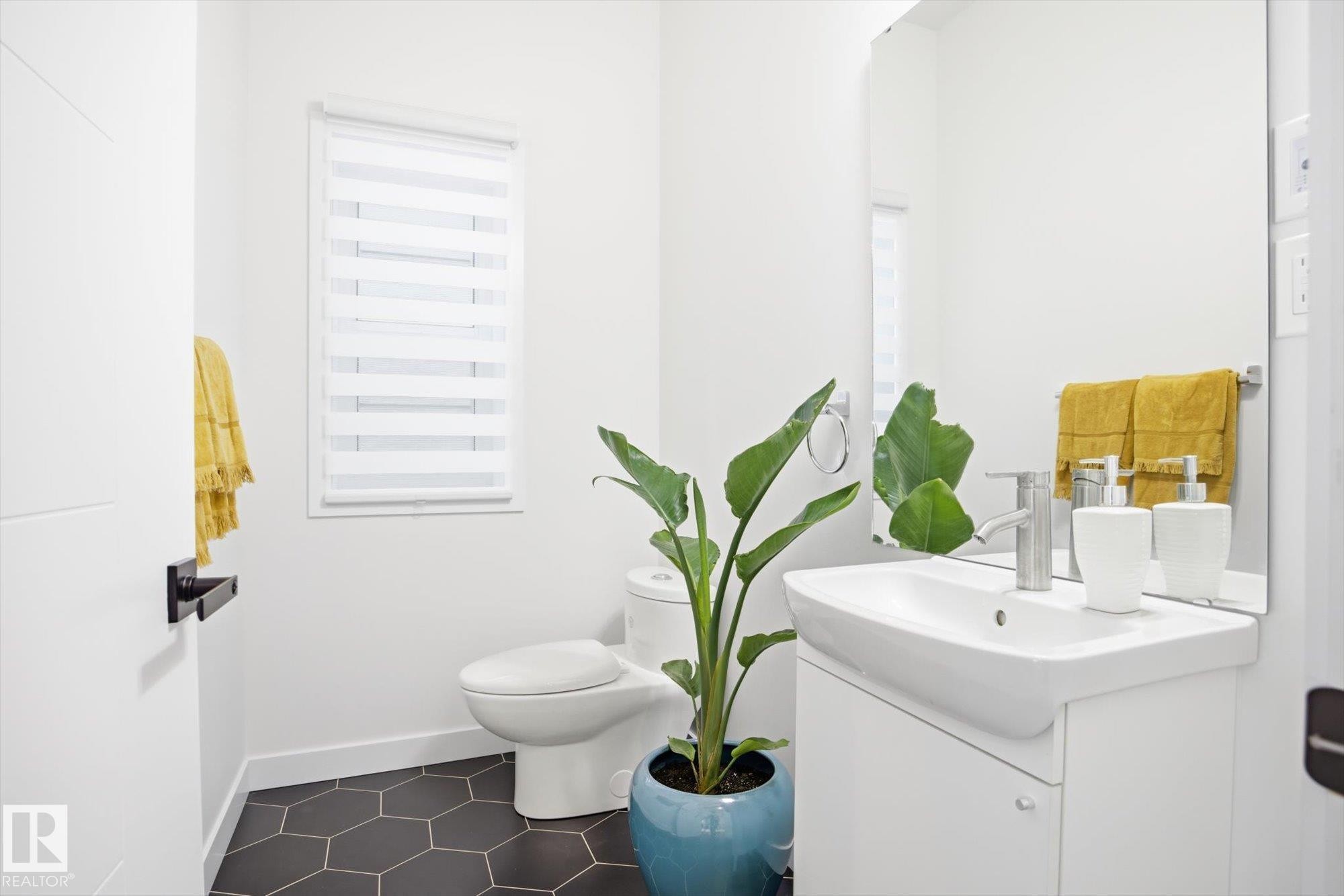 Bathroom featuring a white vanity with an integrated sink, a wall-mounted mirror, a toilet, and hexagon floor tiles - 9821 85 Avenue, Edmonton, AB - Indoor Photo Showing Bathroom
