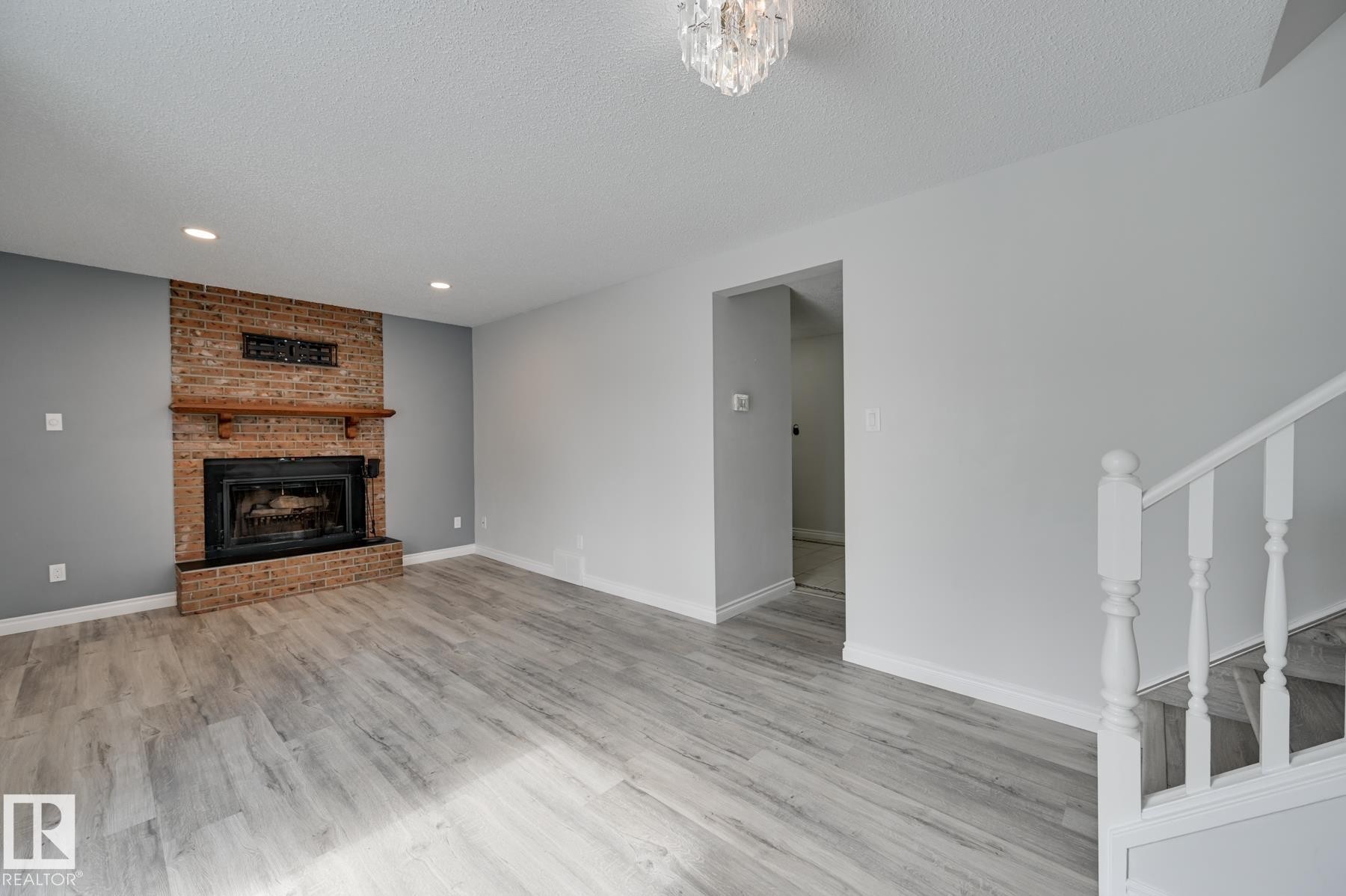 Living area featuring light-toned flooring, a brick fireplace with a wood mantel, and overhead lighting - 8507 152B Avenue, Edmonton, AB - Indoor With Fireplace