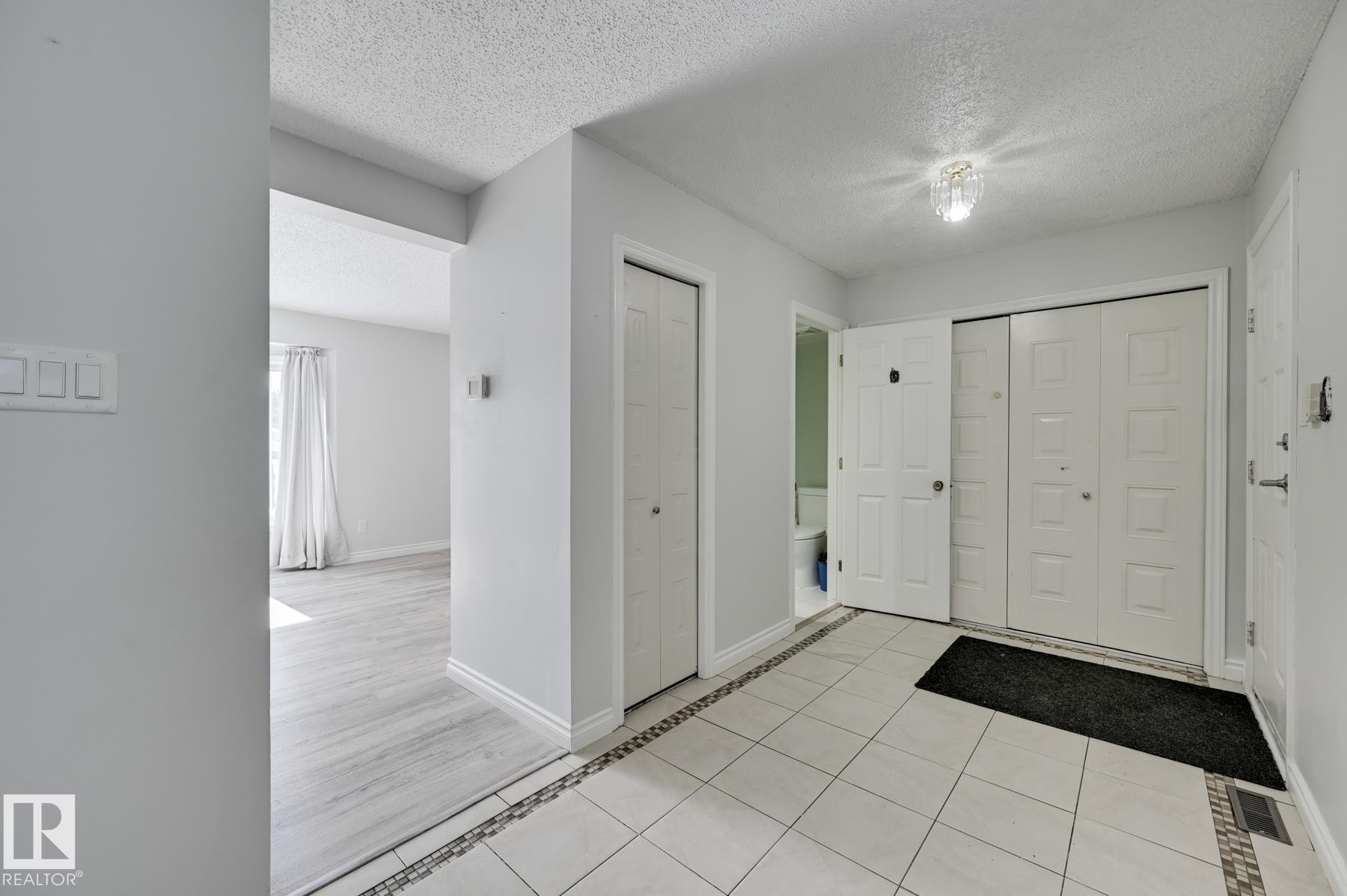 The entryway features light-colored tile flooring with a decorative border, a light fixture, and white bi-fold doors - 8507 152B Avenue, Edmonton, AB - Indoor Photo Showing Other Room