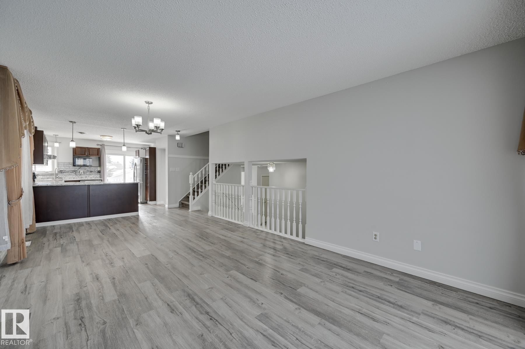 This spacious open-concept area features light grey flooring, freshly painted walls, a modern kitchen with dark cabinetry and stainless steel appliances, and a staircase with white railings - 8507 152B Avenue, Edmonton, AB - Indoor