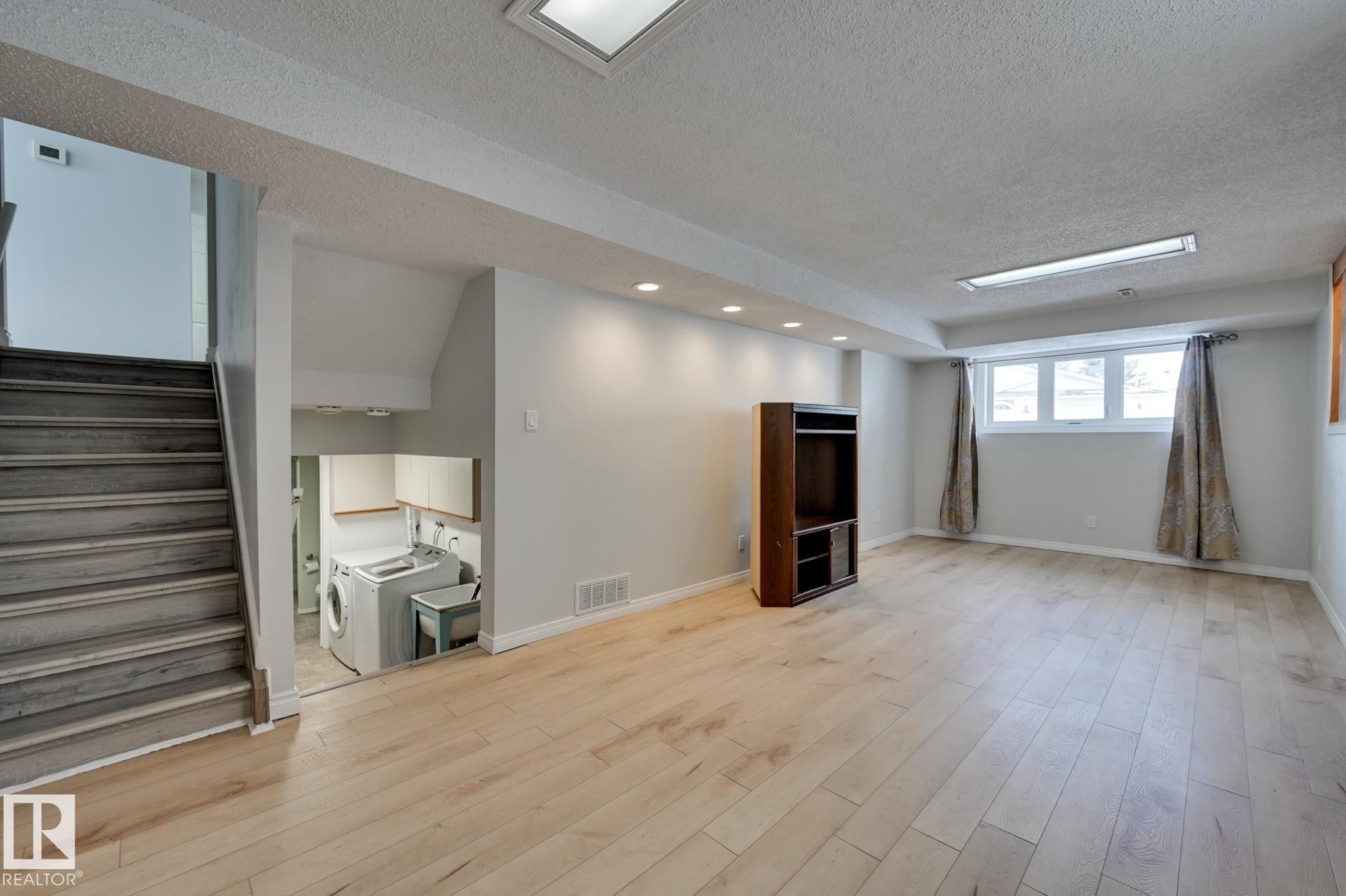 Spacious room featuring light-toned hardwood flooring, recessed lighting, and a window with curtains - 8507 152B Avenue, Edmonton, AB - Indoor Photo Showing Other Room