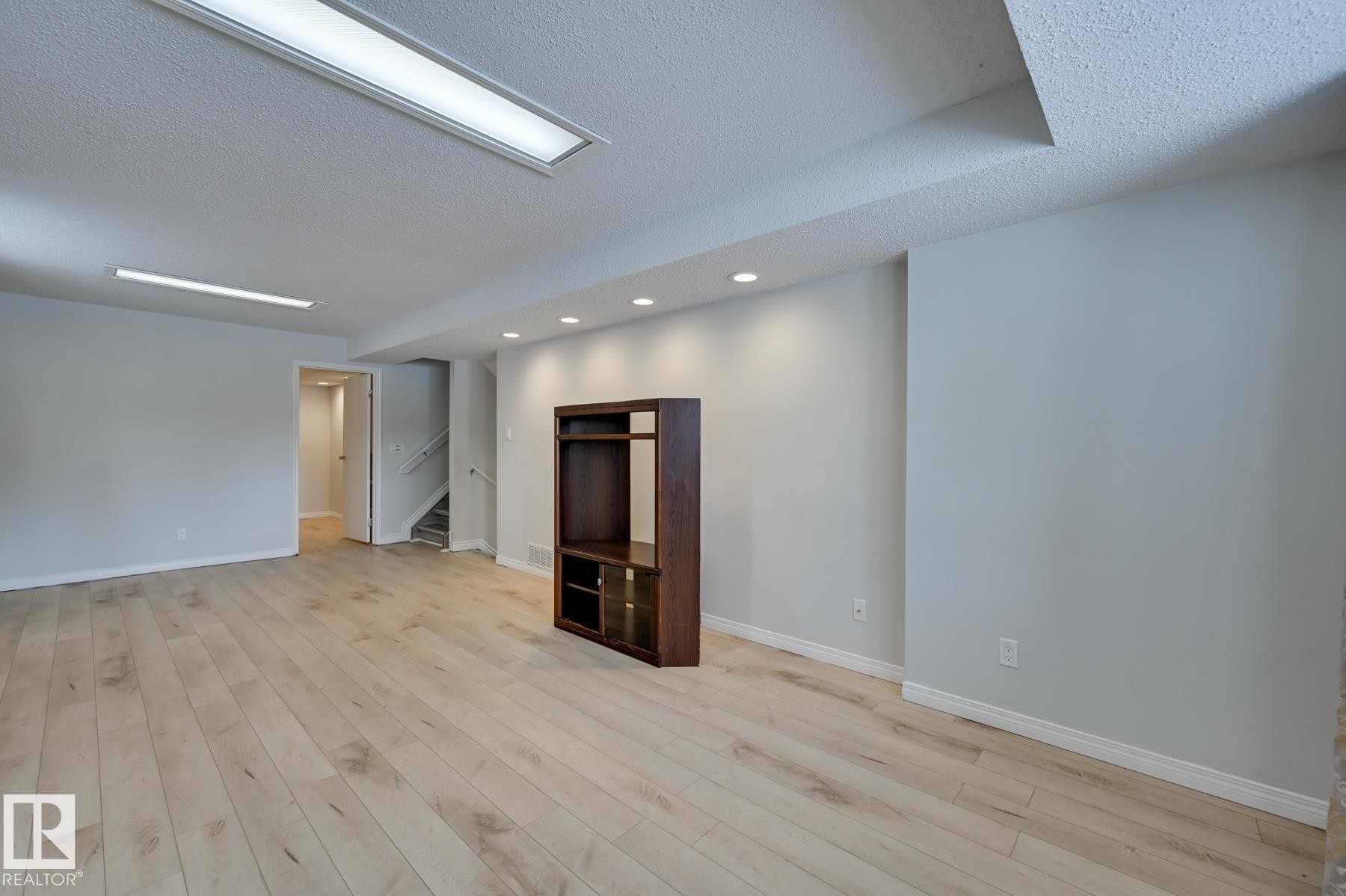 Spacious room featuring light-colored hardwood flooring, light grey walls, and a variety of ceiling lighting including recessed lights and fluorescent fixtures - 8507 152B Avenue, Edmonton, AB - Indoor Photo Showing Other Room