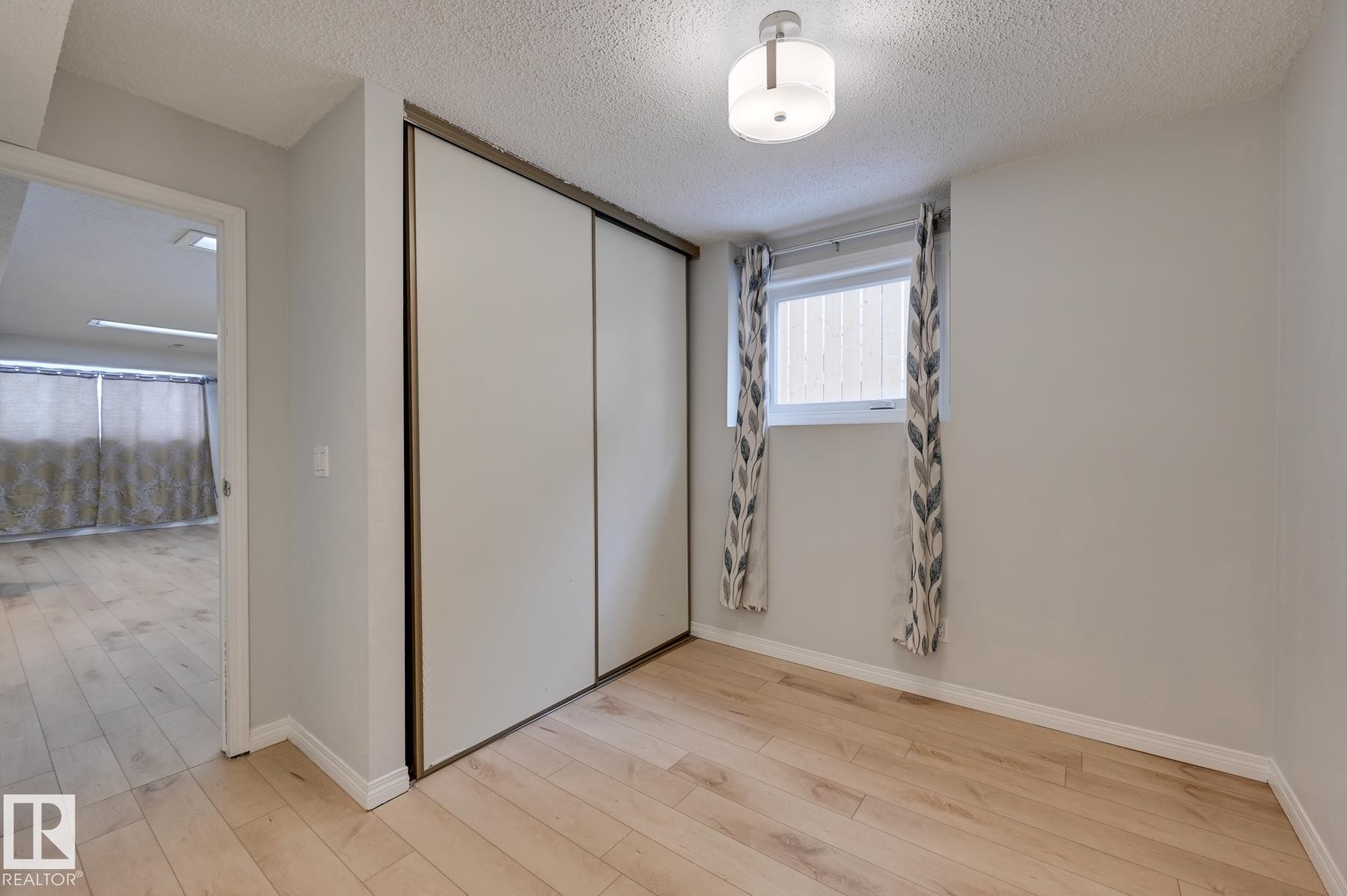 This room features light-toned wood flooring and a window with patterned curtains - 8507 152B Avenue, Edmonton, AB - Indoor Photo Showing Other Room