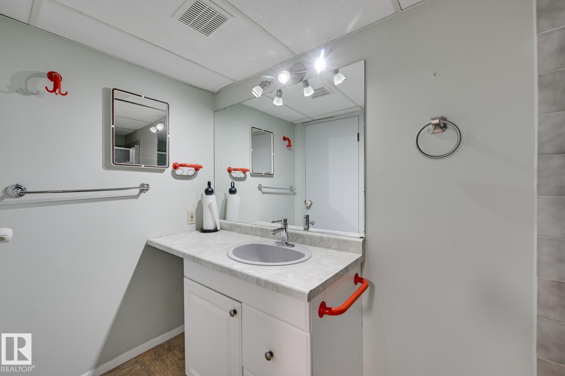 Bathroom featuring a vanity with a countertop, an integrated sink, and a large mirror with overhead lighting - 8507 152B Avenue, Edmonton, AB - Indoor Photo Showing Bathroom