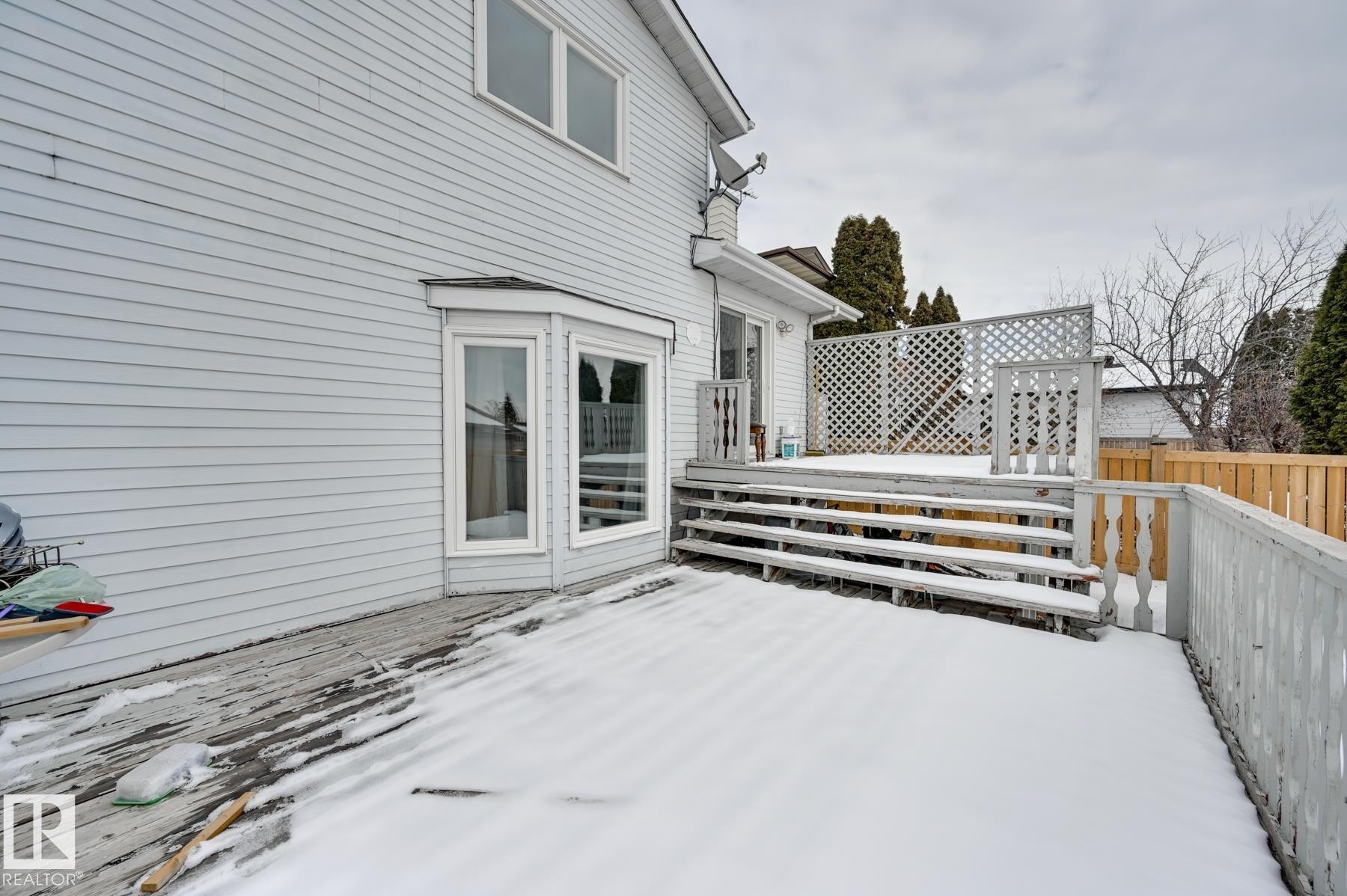 The property features an exterior with light-colored siding, a bay window, and a wooden deck with steps and a lattice privacy screen - 8507 152B Avenue, Edmonton, AB - Outdoor With Exterior