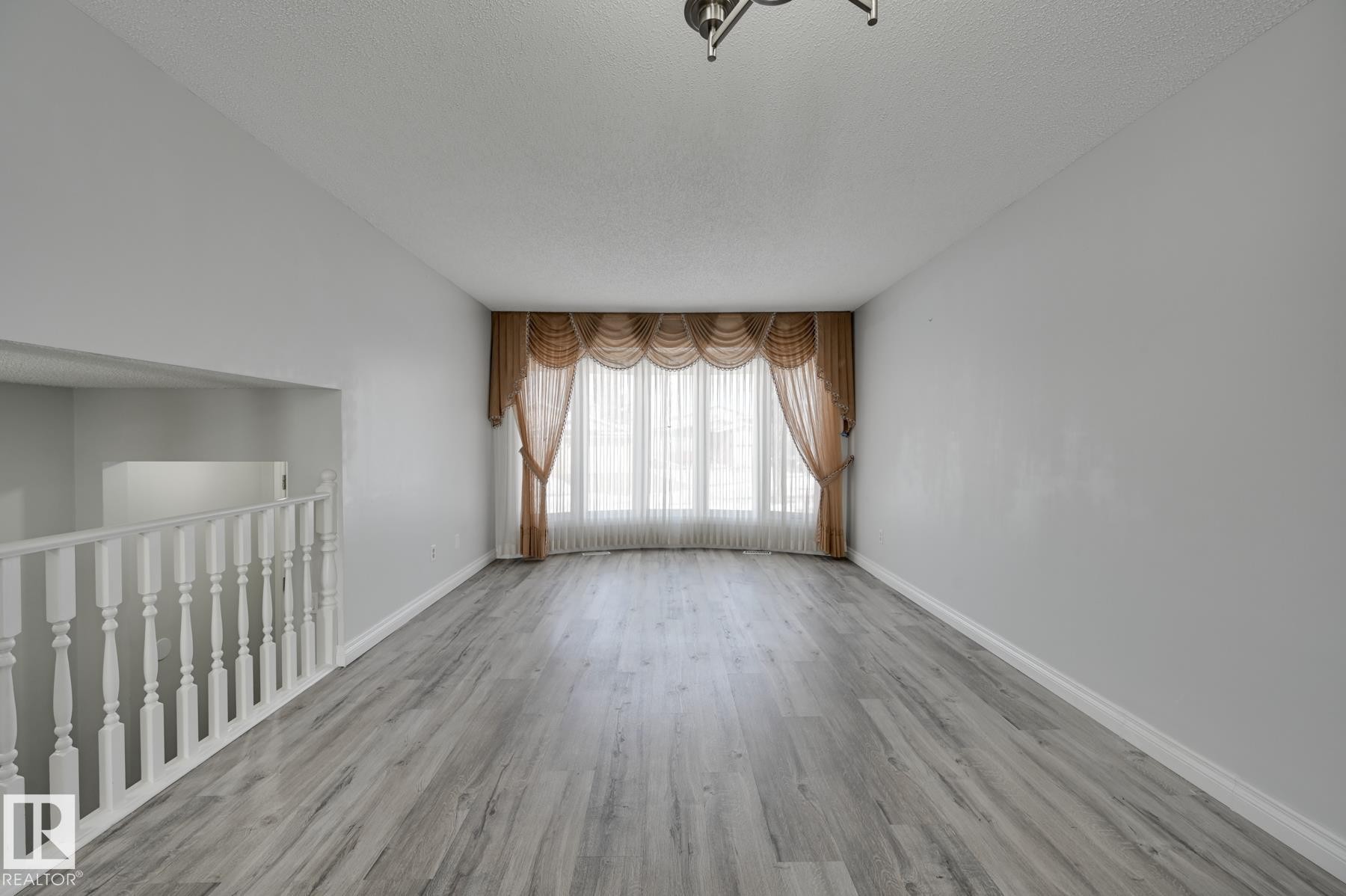The spacious interior features light-toned flooring, light-colored walls, and a window with elegant drapes - 8507 152B Avenue, Edmonton, AB - Indoor Photo Showing Other Room