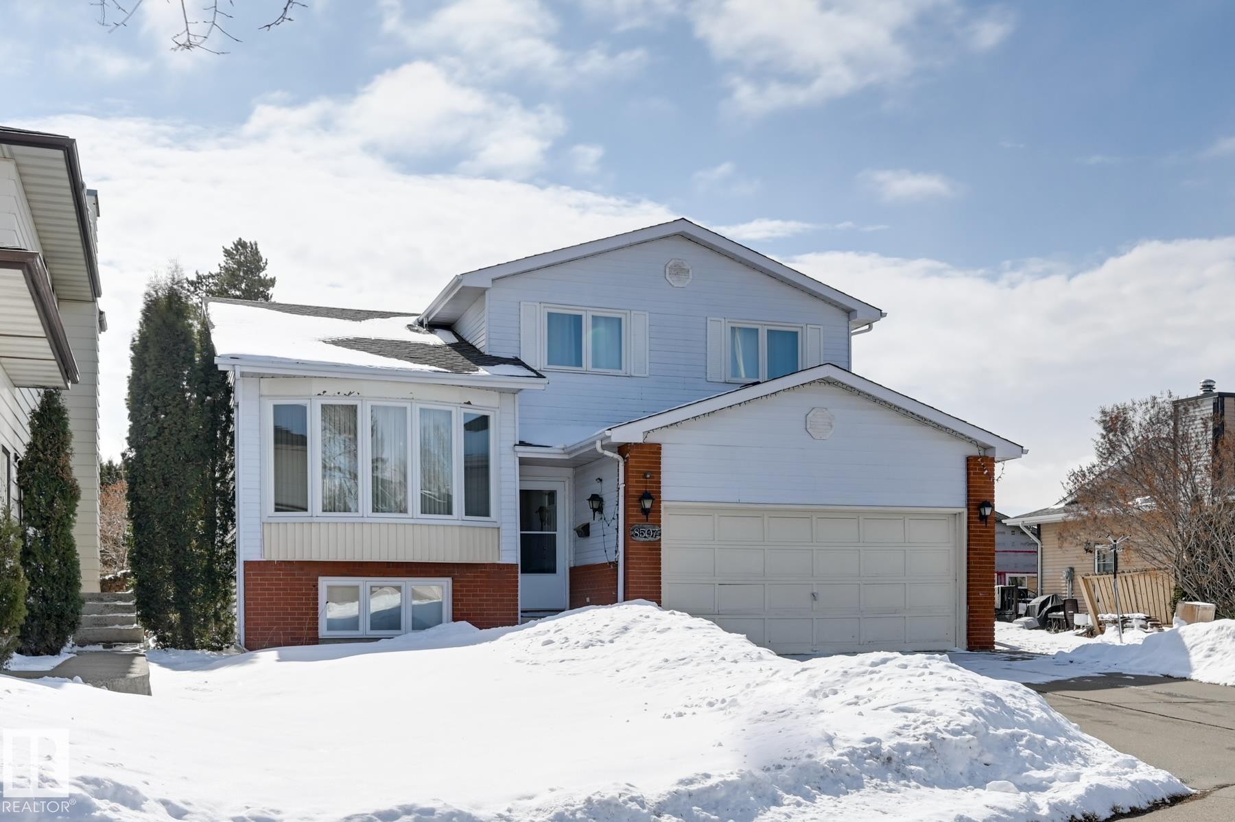 The property features a two-story exterior with white siding and brick accents, an integrated garage, and a bay window - 8507 152B Avenue, Edmonton, AB - Outdoor With Facade