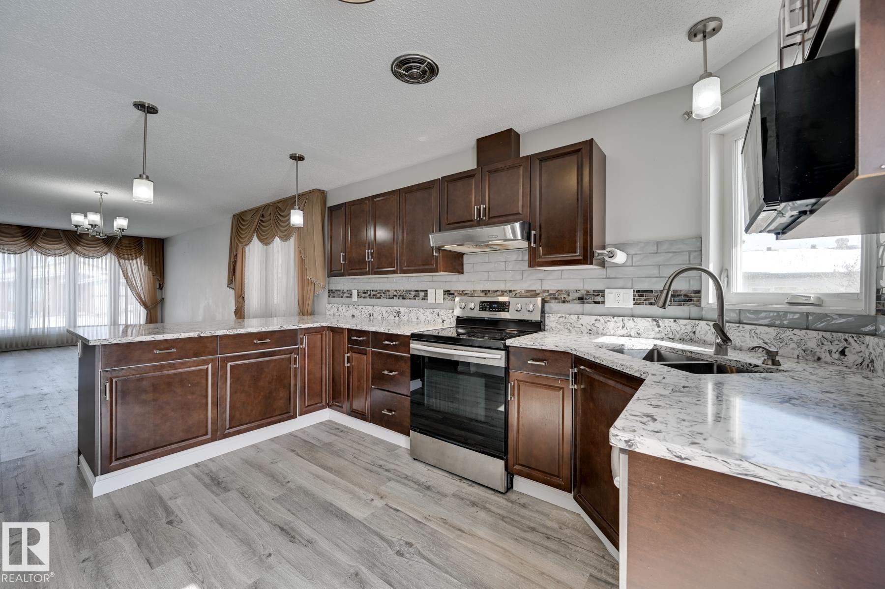 The kitchen features hardwood cabinetry, granite countertops, and stainless steel appliances, with a light gray backsplash and a sink with a gooseneck faucet - 8507 152B Avenue, Edmonton, AB - Indoor Photo Showing Kitchen With Double Sink With Upgraded Kitchen
