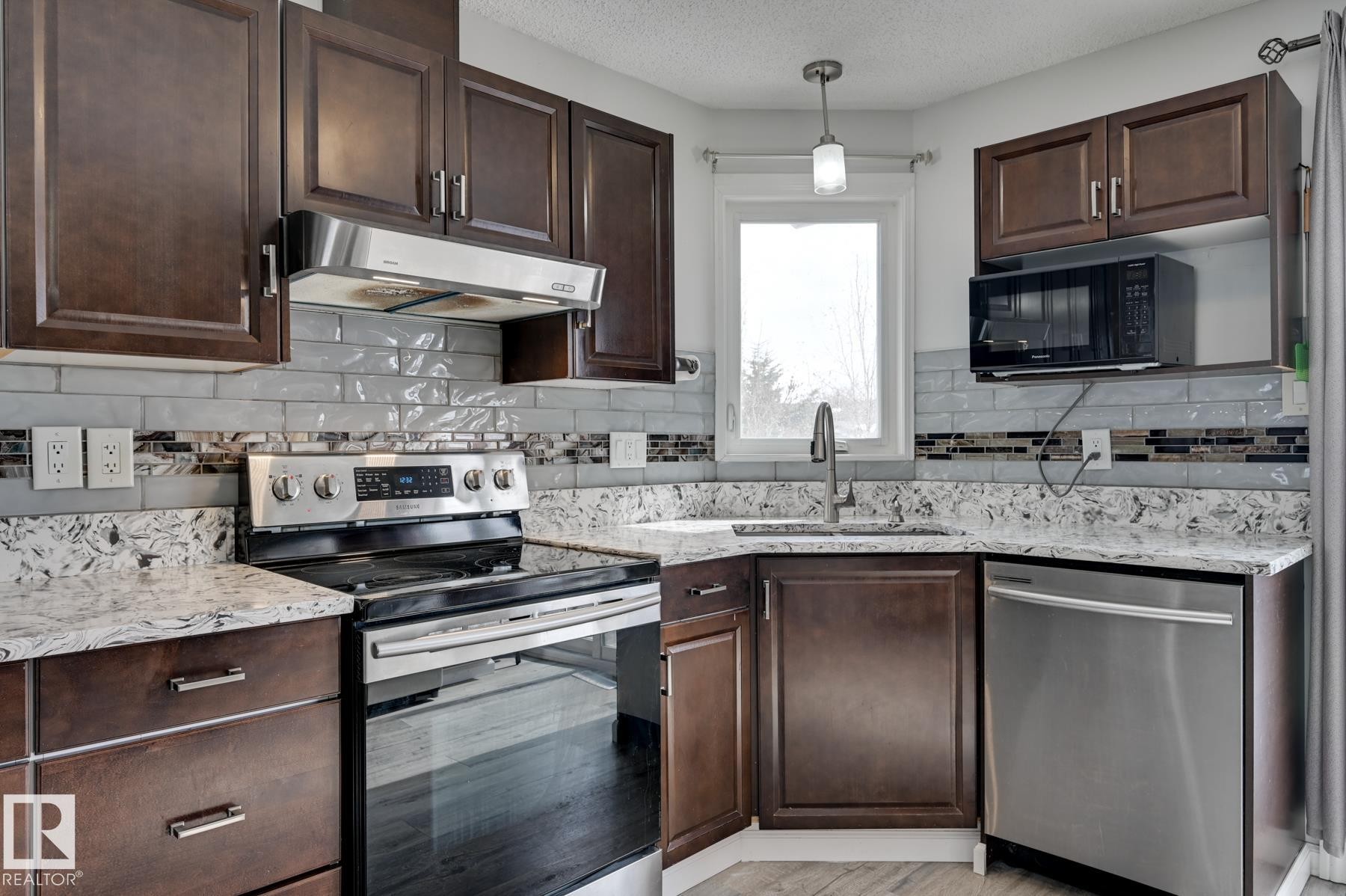 The kitchen features dark wood cabinetry, light-colored granite countertops, and a subway tile backsplash - 8507 152B Avenue, Edmonton, AB - Indoor Photo Showing Kitchen With Stainless Steel Kitchen