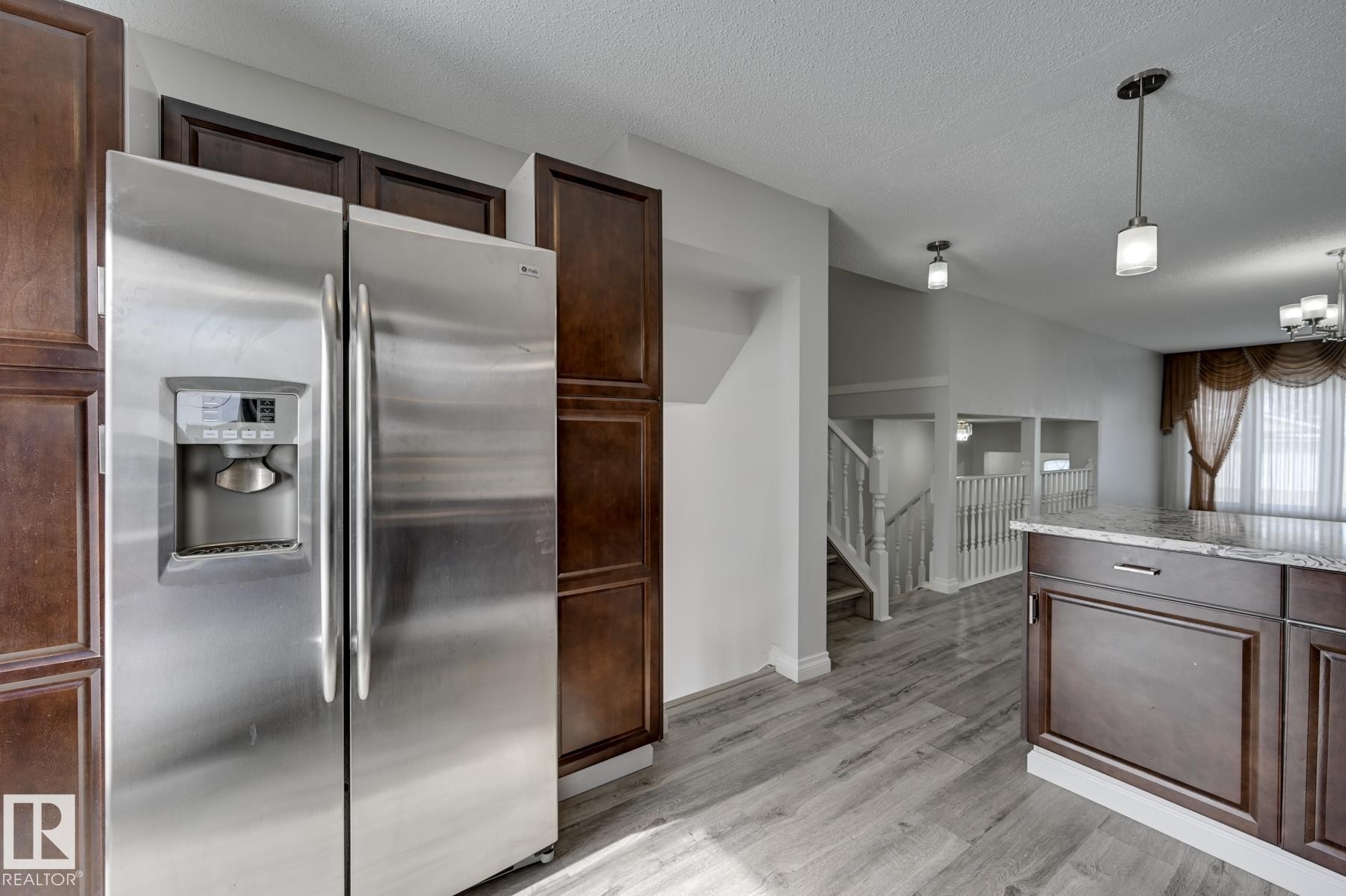 The kitchen features dark wood cabinetry, a stainless steel refrigerator with a dispenser, and a kitchen island with a granite countertop - 8507 152B Avenue, Edmonton, AB - Indoor Photo Showing Kitchen