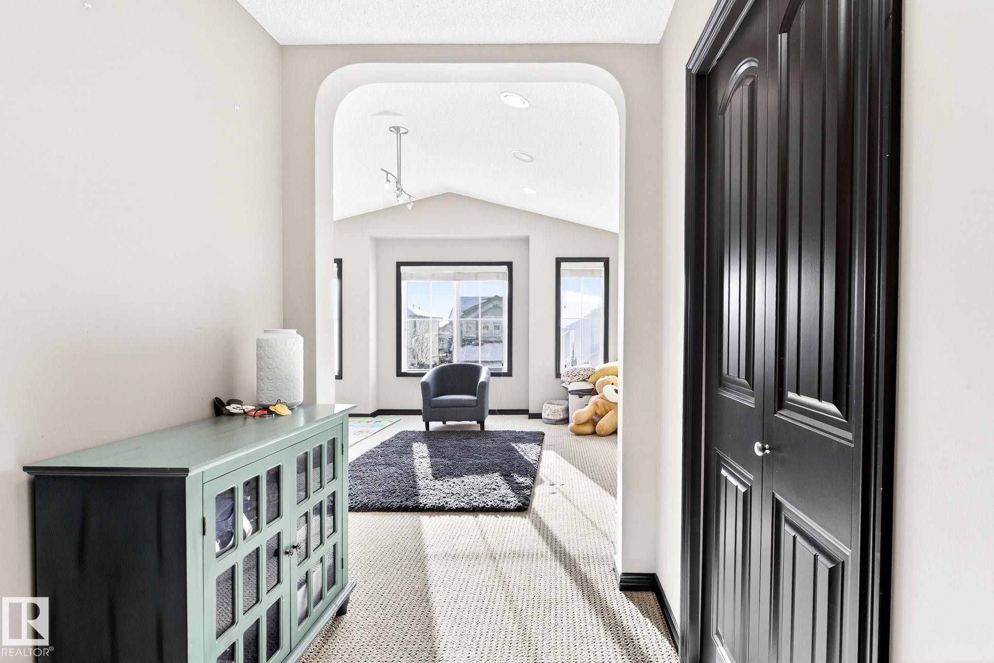 Bright hallway with light-colored walls and a textured carpet, leading to an open living area with large windows, a vaulted ceiling, and recessed lighting - 1121 59A Street, Edmonton, AB - Indoor Photo Showing Other Room