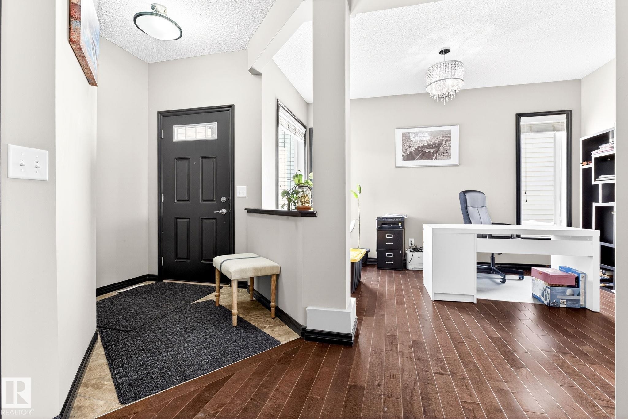 The property features a welcoming entryway with a dark paneled door and light-colored walls, leading to a room with rich hardwood flooring - 1121 59A Street, Edmonton, AB - Indoor Photo Showing Other Room