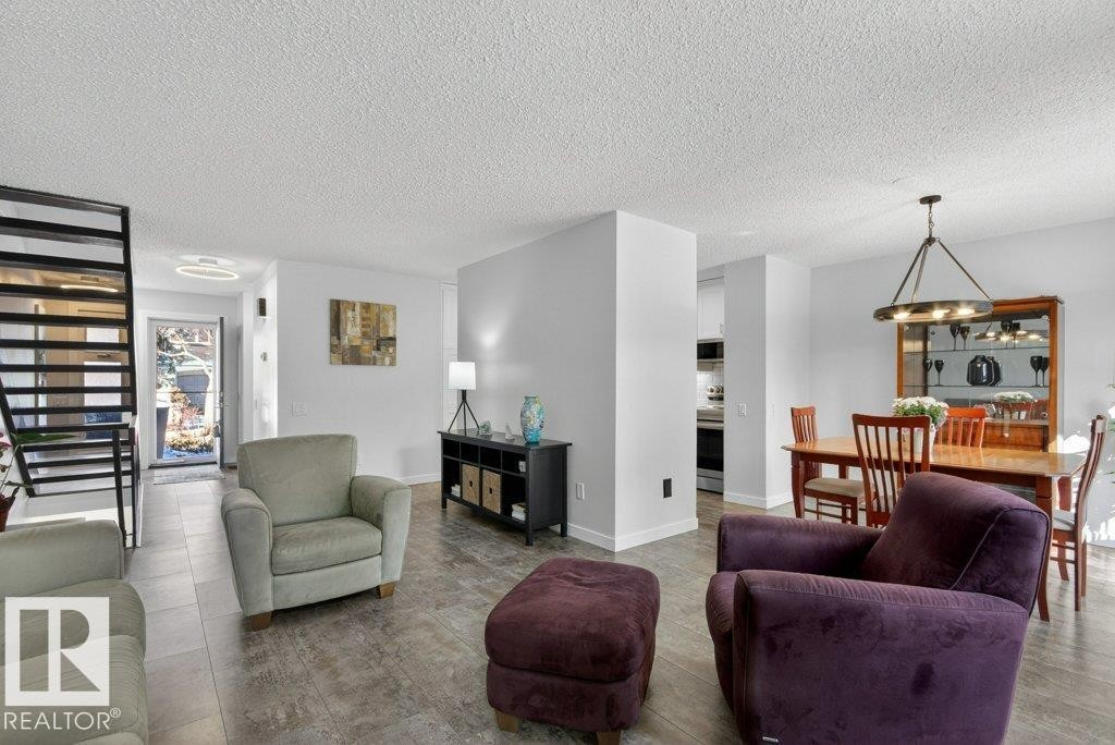 The property features an open-concept living area with luxury vinyl tile flooring, a staircase with black railings, and a dining area illuminated by an overhead chandelier - 91 Hearthstone, Edmonton, AB - Indoor Photo Showing Living Room