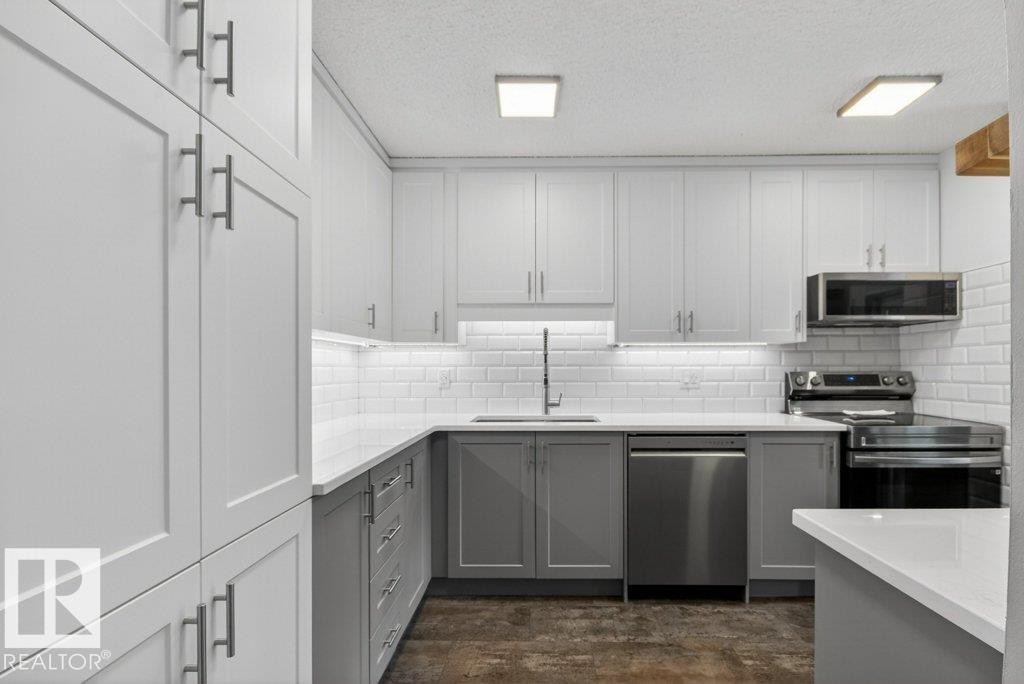 The kitchen features white shaker-style upper cabinets and gray lower cabinets, complemented by quartz countertops and a subway tile backsplash - 91 Hearthstone, Edmonton, AB - Indoor Photo Showing Kitchen With Stainless Steel Kitchen With Upgraded Kitchen