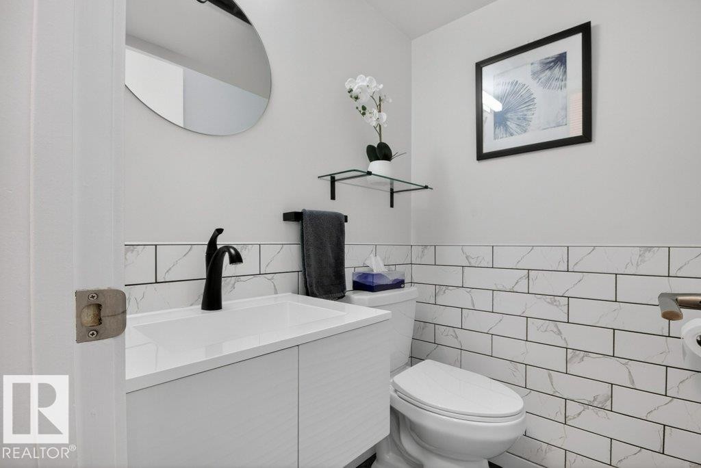 The guest bathroom features a modern vanity with a white countertop and a black faucet, complemented by a round mirror - 91 Hearthstone, Edmonton, AB - Indoor Photo Showing Bathroom