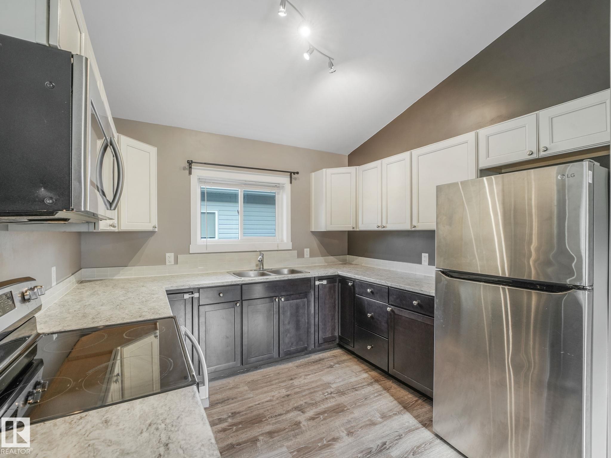 The kitchen features a stainless steel refrigerator, dark base cabinets, white upper cabinets, and a window above the sink - 5035 51 Avenue, Lamont, AB - Indoor Photo Showing Kitchen With Stainless Steel Kitchen With Double Sink