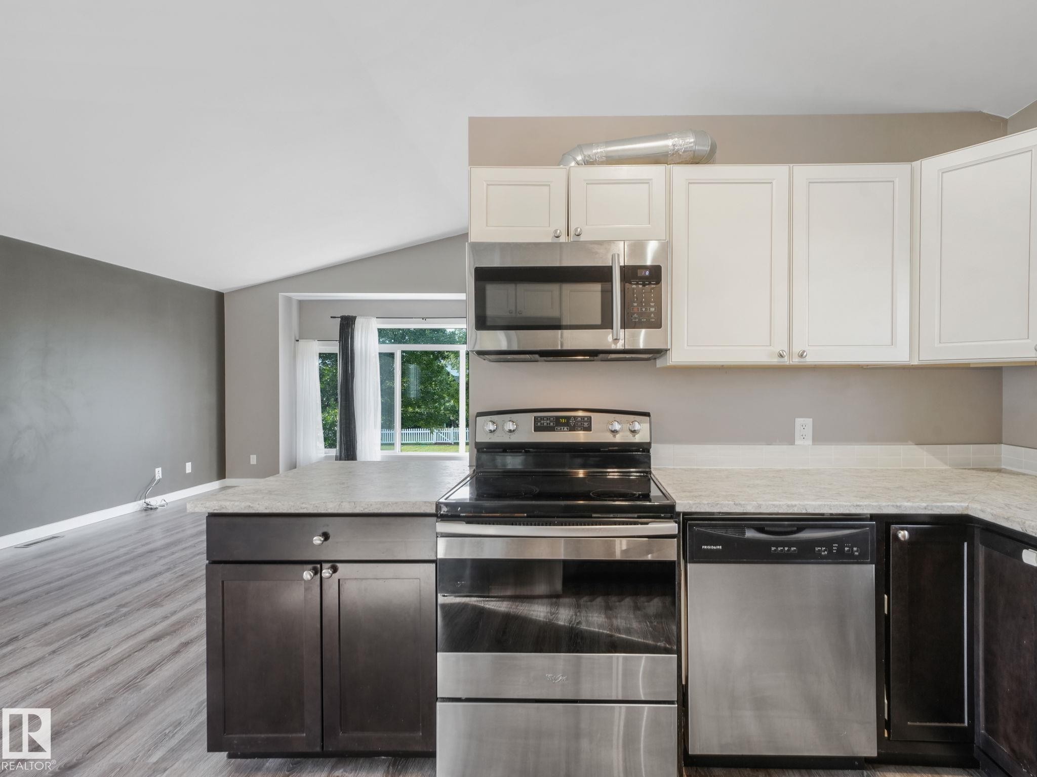 The kitchen features white upper cabinetry, dark lower cabinetry, and stainless steel appliances including a microwave, oven with a stovetop, and a dishwasher - 5035 51 Avenue, Lamont, AB - Indoor Photo Showing Kitchen