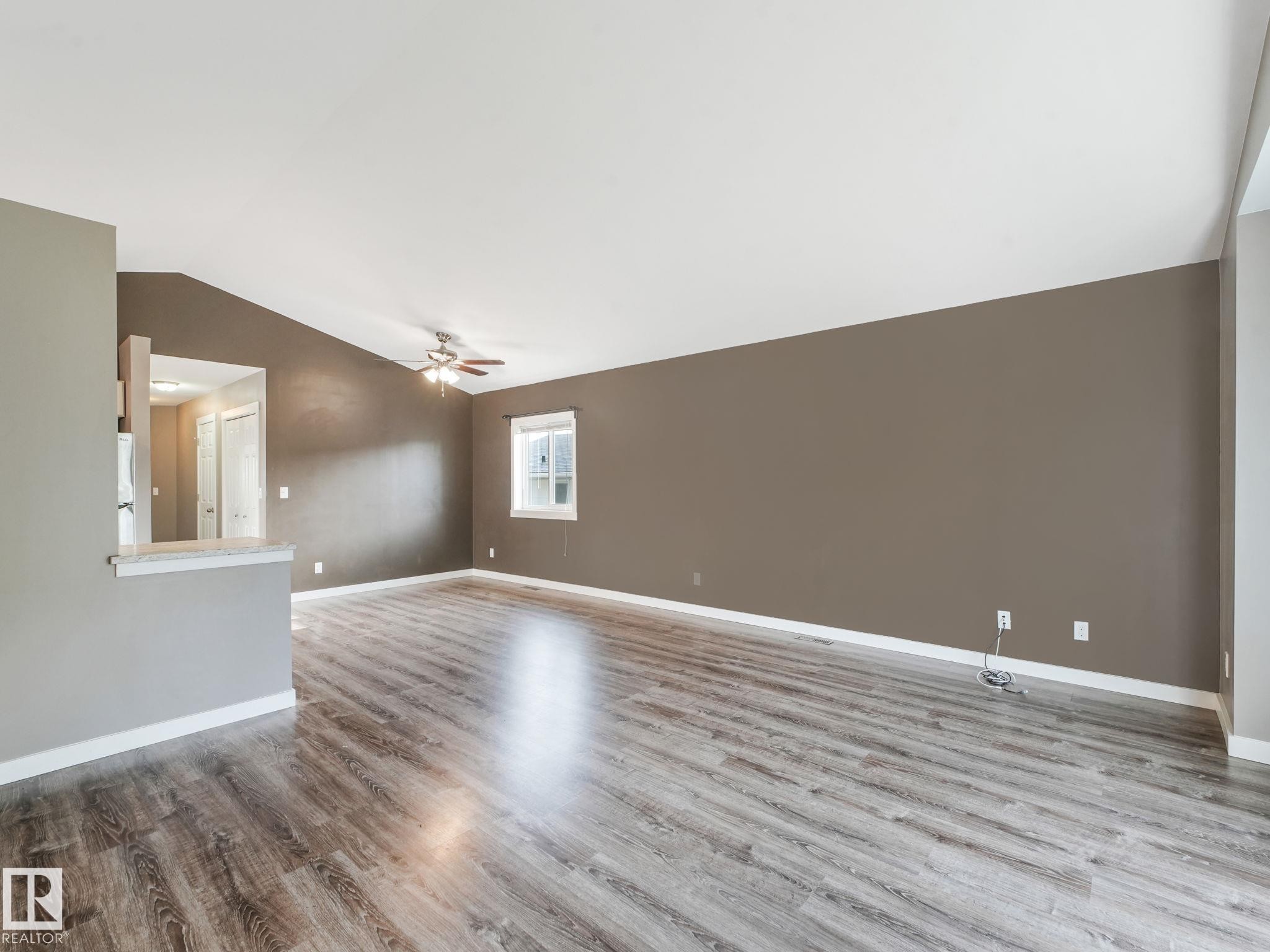 The property features a spacious room with wood-style flooring, a vaulted ceiling, and a ceiling fan - 5035 51 Avenue, Lamont, AB - Indoor Photo Showing Other Room