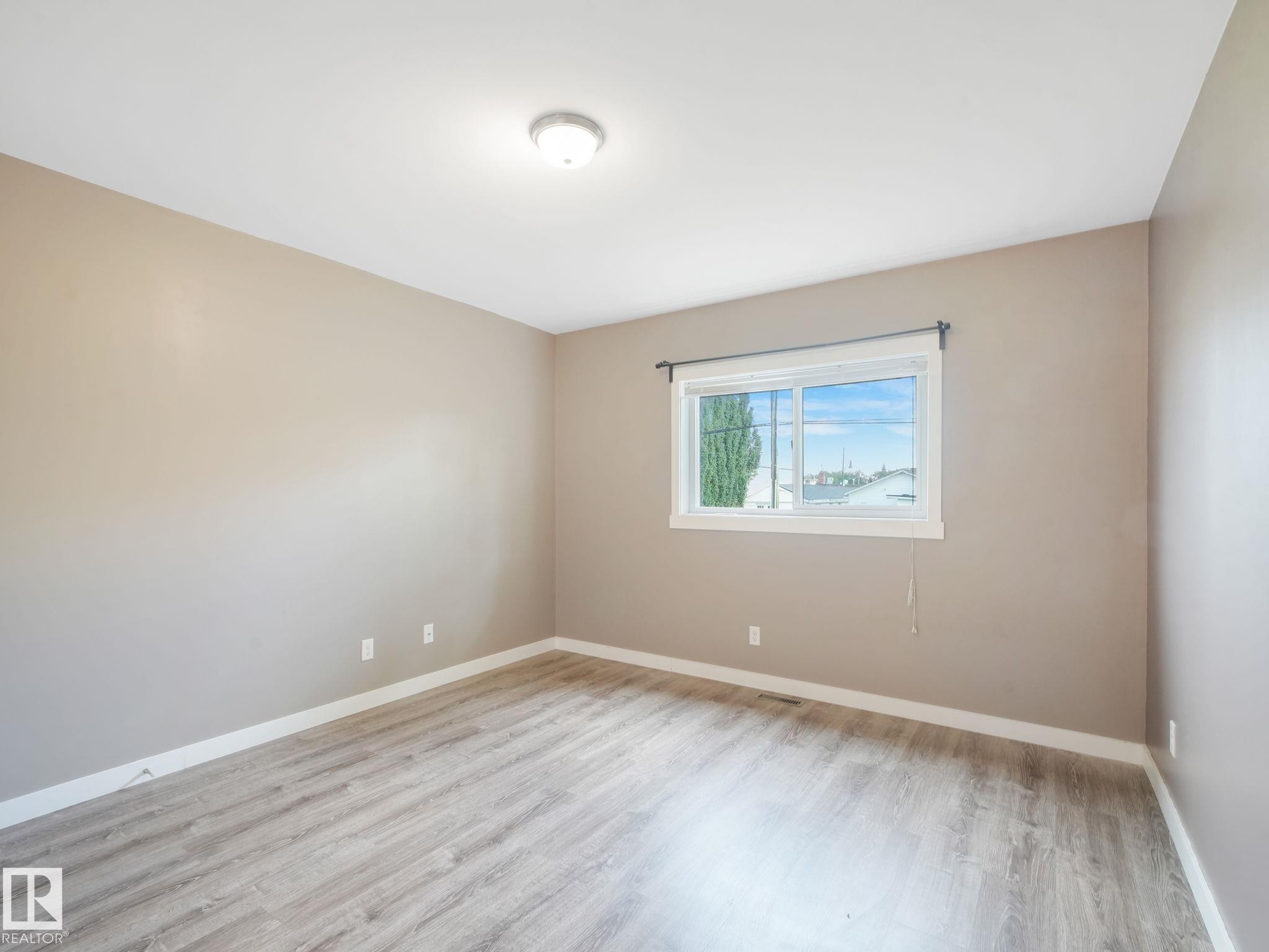 The room features neutral-toned walls, wood-look flooring, and a window with a view of the surrounding area - 5035 51 Avenue, Lamont, AB - Indoor Photo Showing Other Room