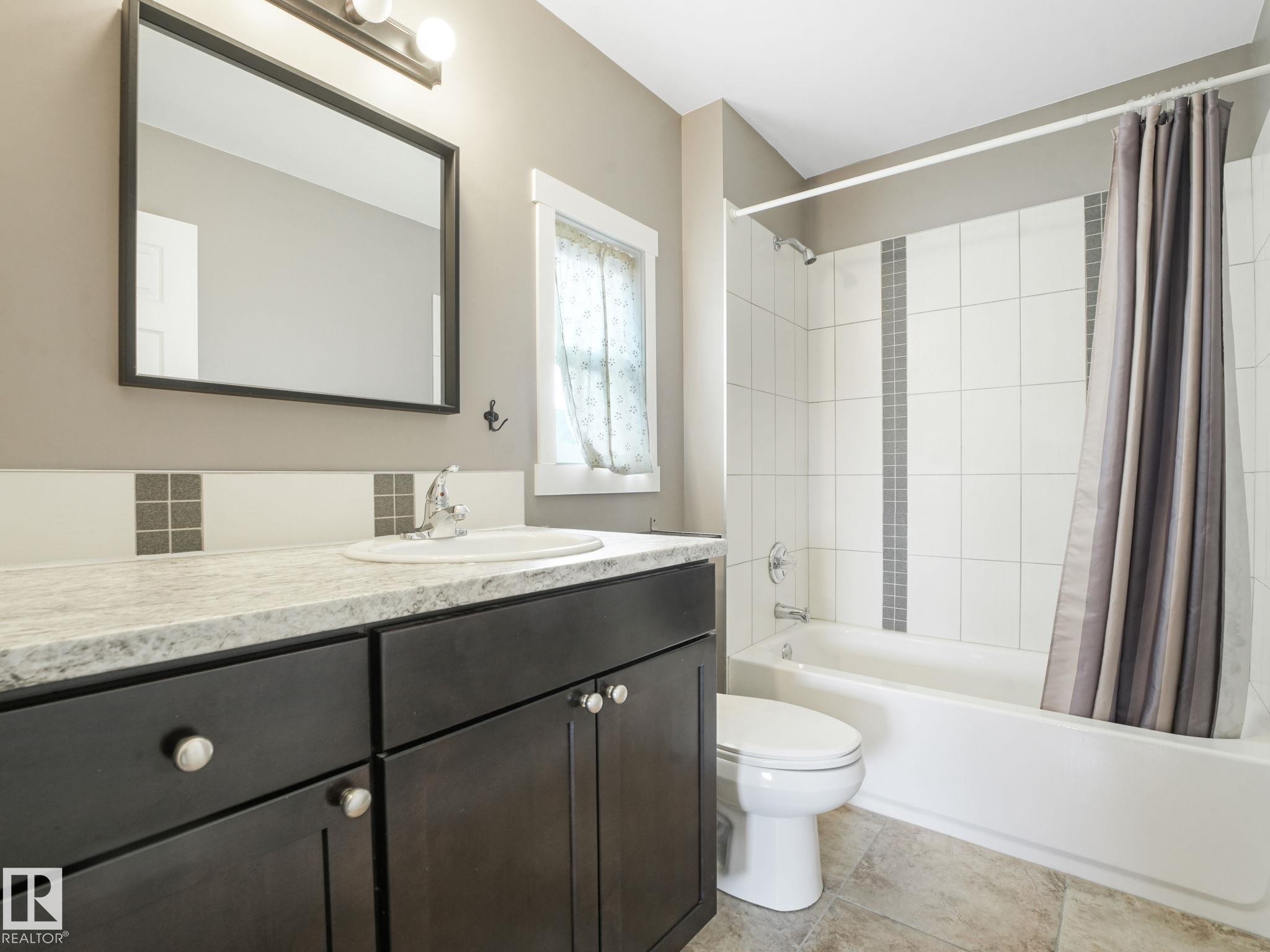 The bathroom features a vanity with dark cabinetry, a countertop with an integrated sink, and a framed mirror above - 5035 51 Avenue, Lamont, AB - Indoor Photo Showing Bathroom
