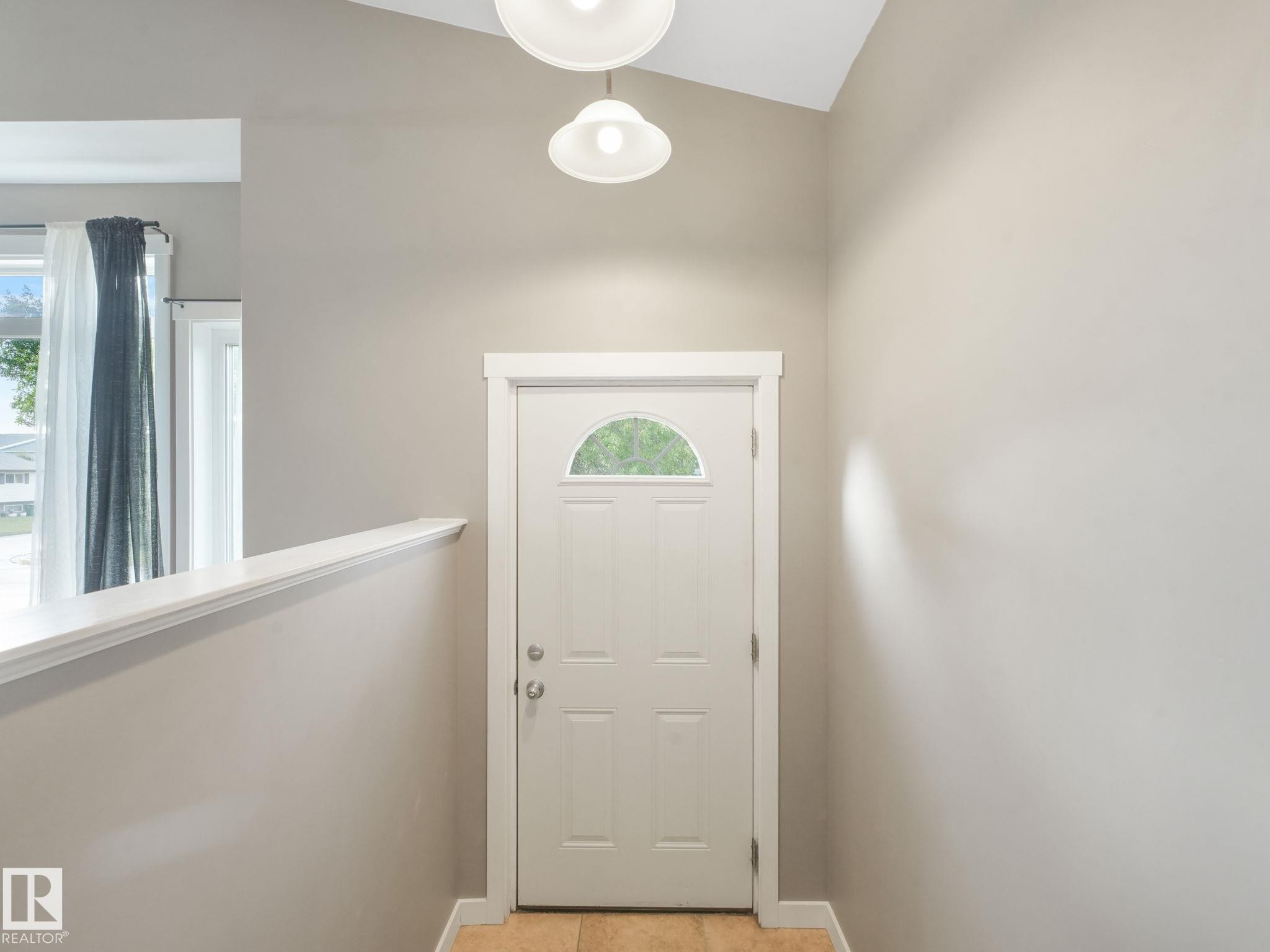 The property features a white paneled door with an arched window, complemented by light-colored walls and a vaulted ceiling - 5035 51 Avenue, Lamont, AB - Indoor Photo Showing Other Room