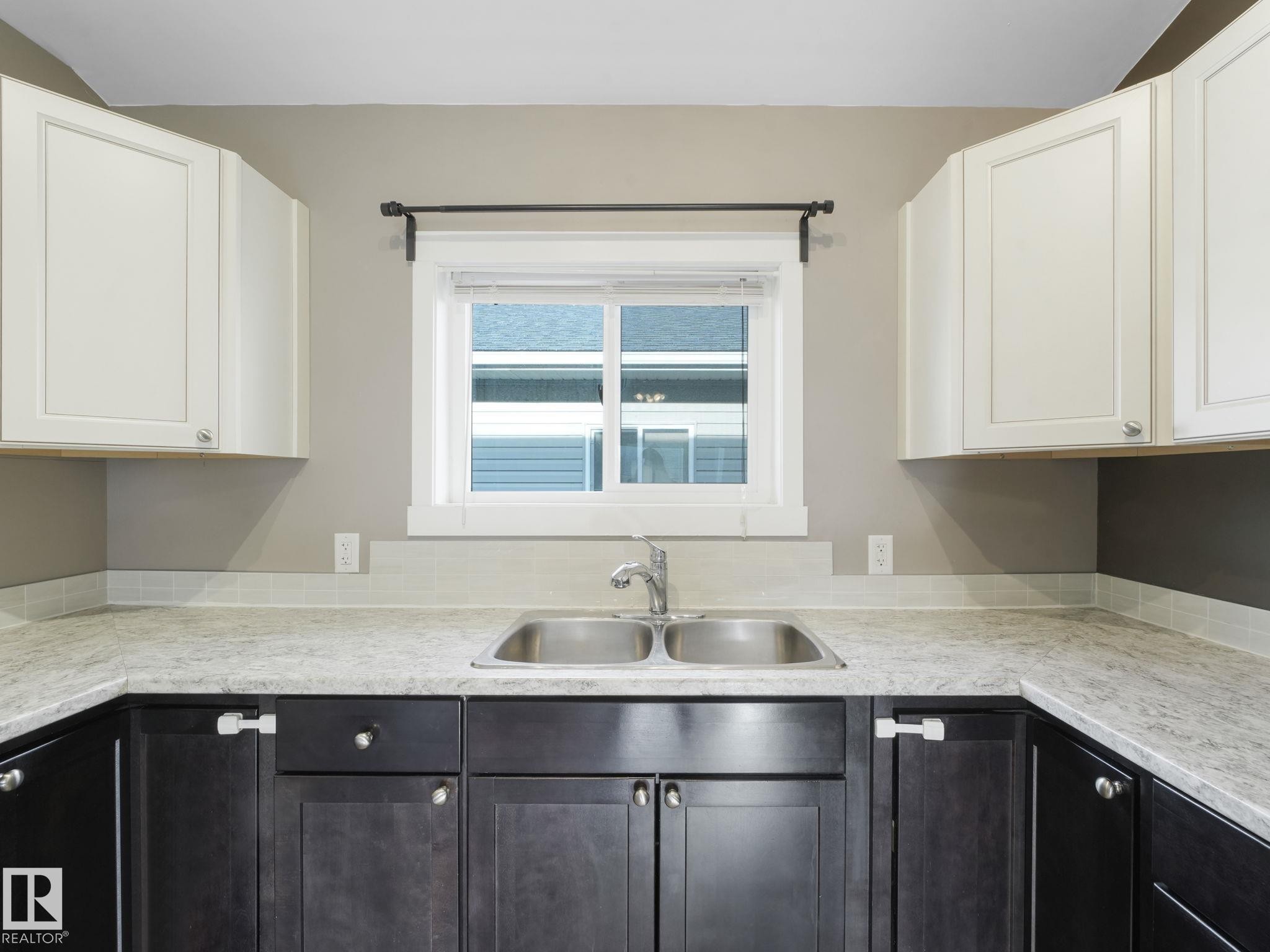 Kitchen featuring a double basin stainless steel sink, light countertops, and cabinetry with both light and dark finishes - 5035 51 Avenue, Lamont, AB - Indoor Photo Showing Kitchen With Double Sink