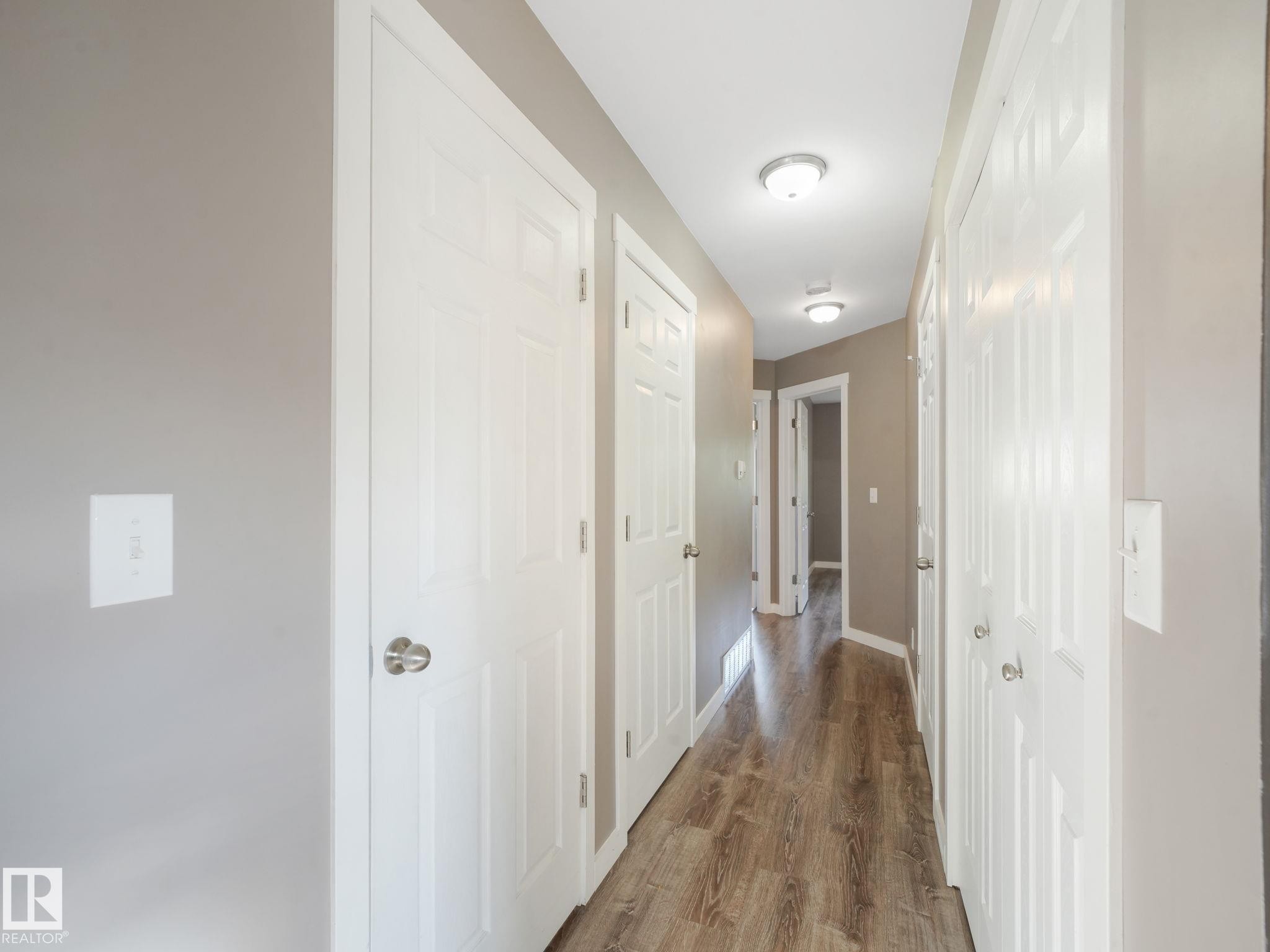 The property features a hallway with wood-look flooring and white paneled doors - 5035 51 Avenue, Lamont, AB - Indoor Photo Showing Other Room