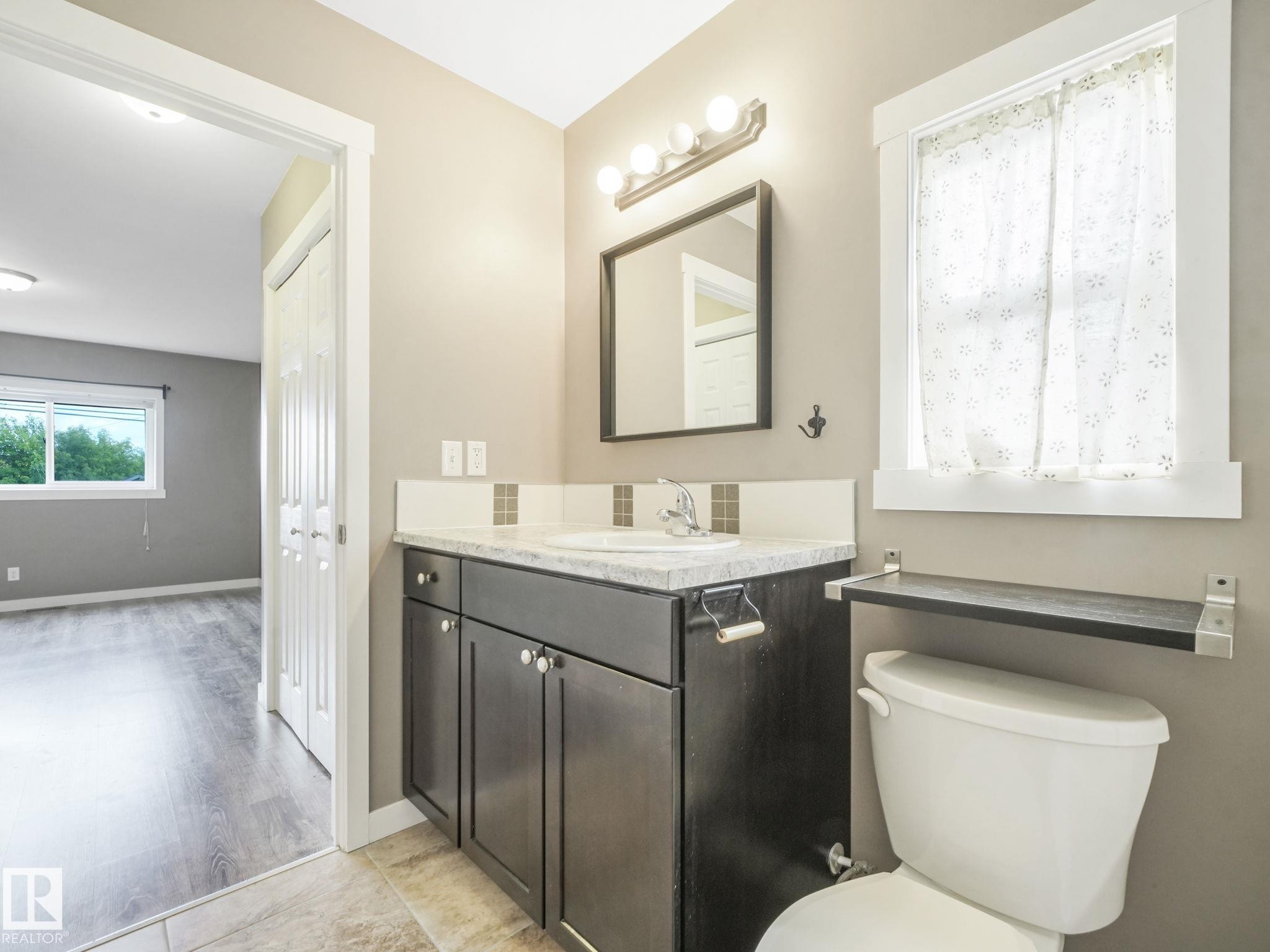 This bathroom features a vanity with a white countertop and a rectangular sink, complemented by a mirror and overhead lighting - 5035 51 Avenue, Lamont, AB - Indoor Photo Showing Bathroom