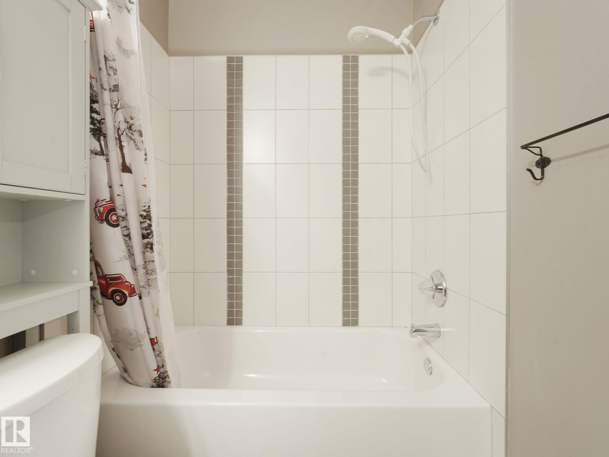 Bathroom featuring a bathtub with a shower, white tiled walls with a decorative accent strip, and a chrome shower fixture - 5035 51 Avenue, Lamont, AB - Indoor Photo Showing Bathroom