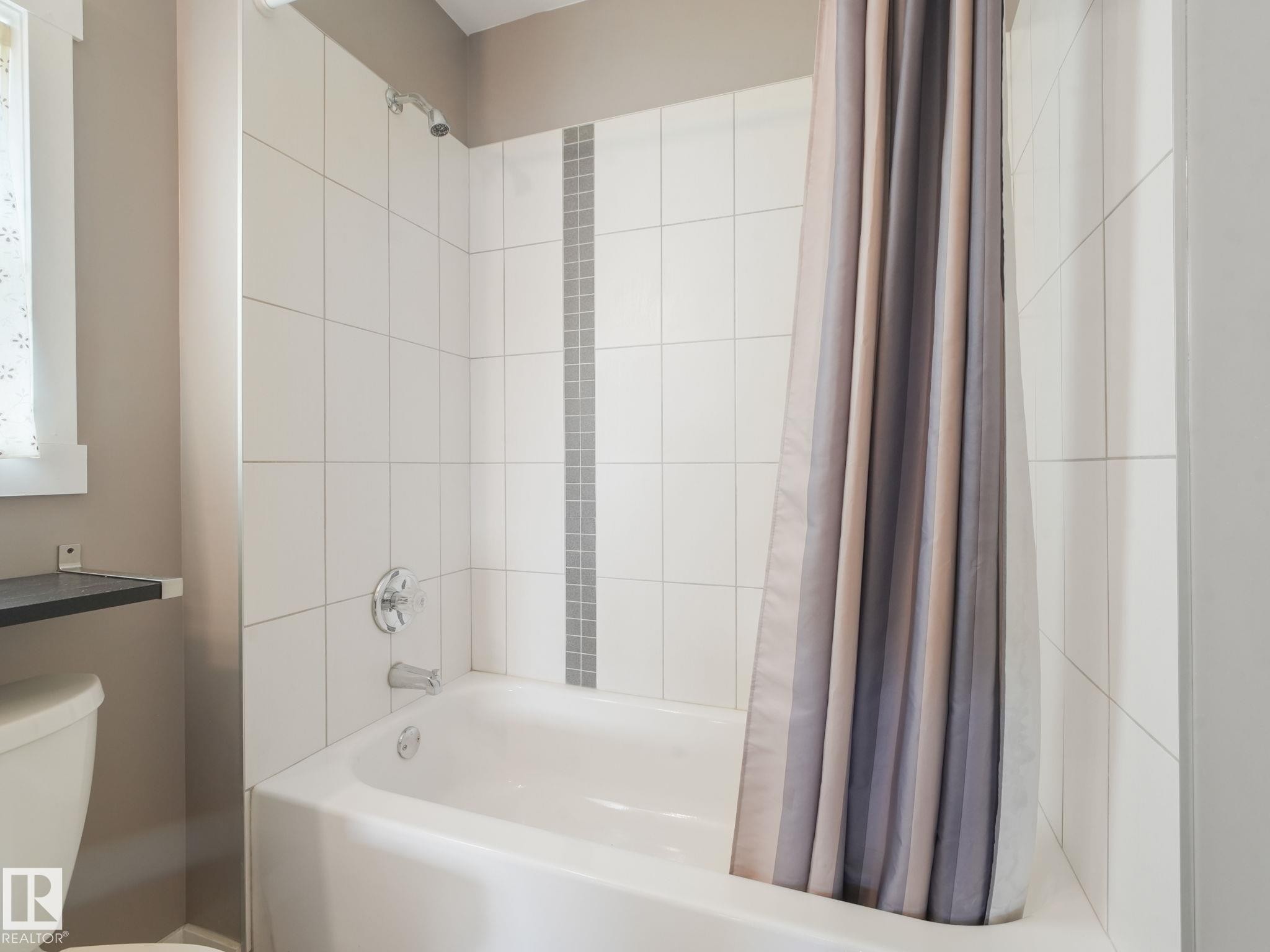 Bathroom featuring a white bathtub with chrome fixtures and white tiled walls - 5035 51 Avenue, Lamont, AB - Indoor Photo Showing Bathroom