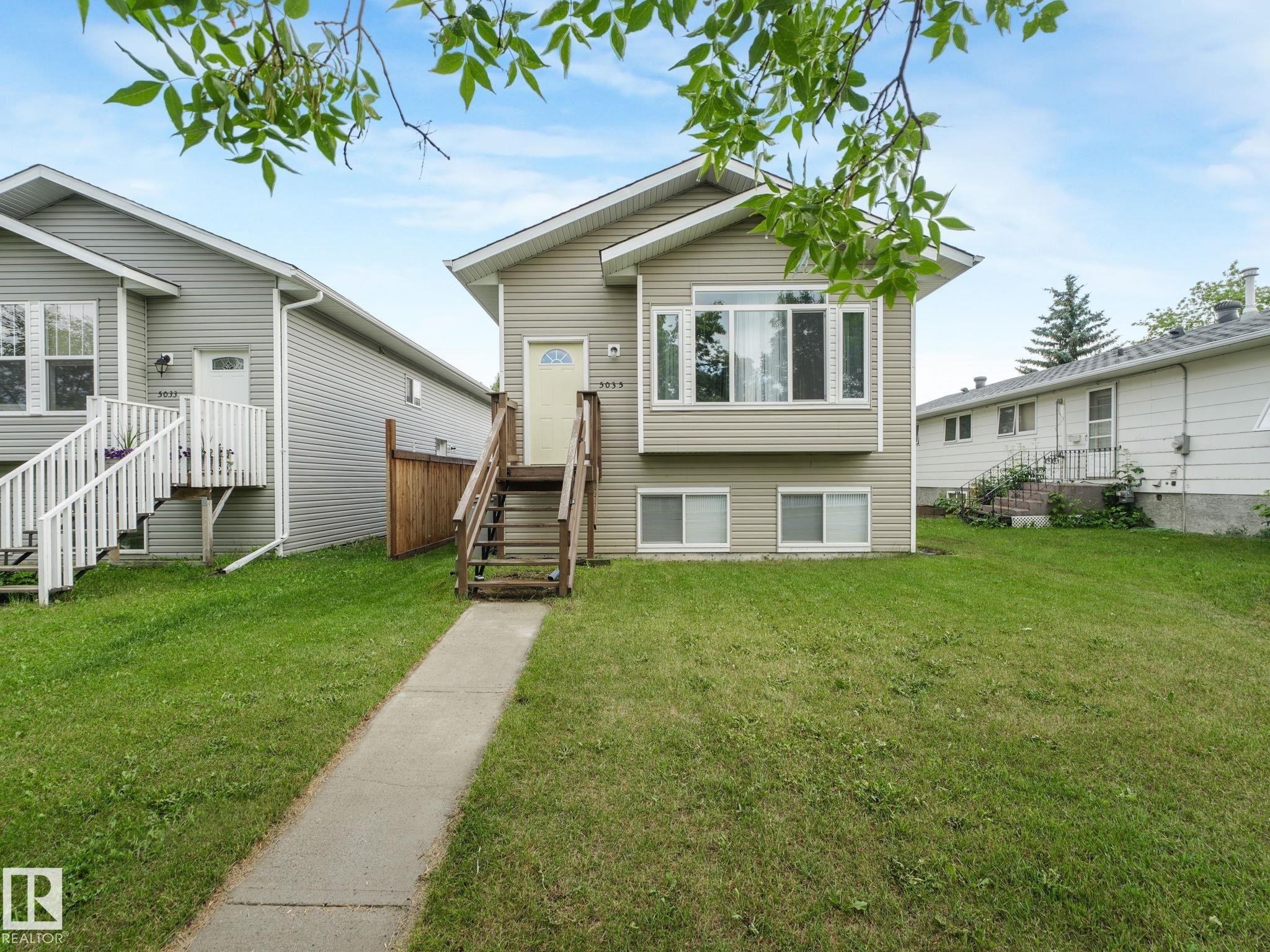 The property features a large front lawn and a concrete walkway leading to the entrance, which is accessed via wooden steps - 5035 51 Avenue, Lamont, AB - Outdoor