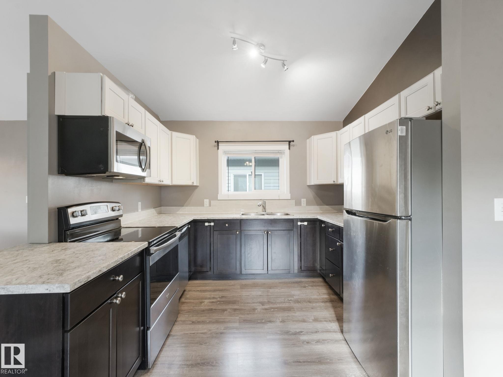 The kitchen features a U-shaped layout with light-colored countertops, dark lower cabinetry, and light upper cabinetry - 5035 51 Avenue, Lamont, AB - Indoor Photo Showing Kitchen With Stainless Steel Kitchen