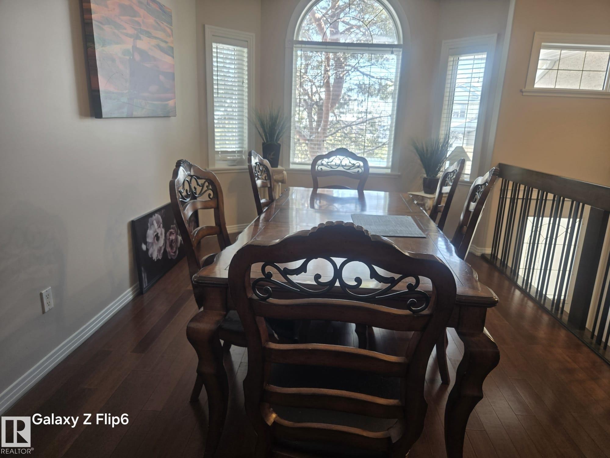 This dining area features hardwood floors and a large arched window with blinds, allowing for natural light - Edmonton, AB - Indoor Photo Showing Dining Room