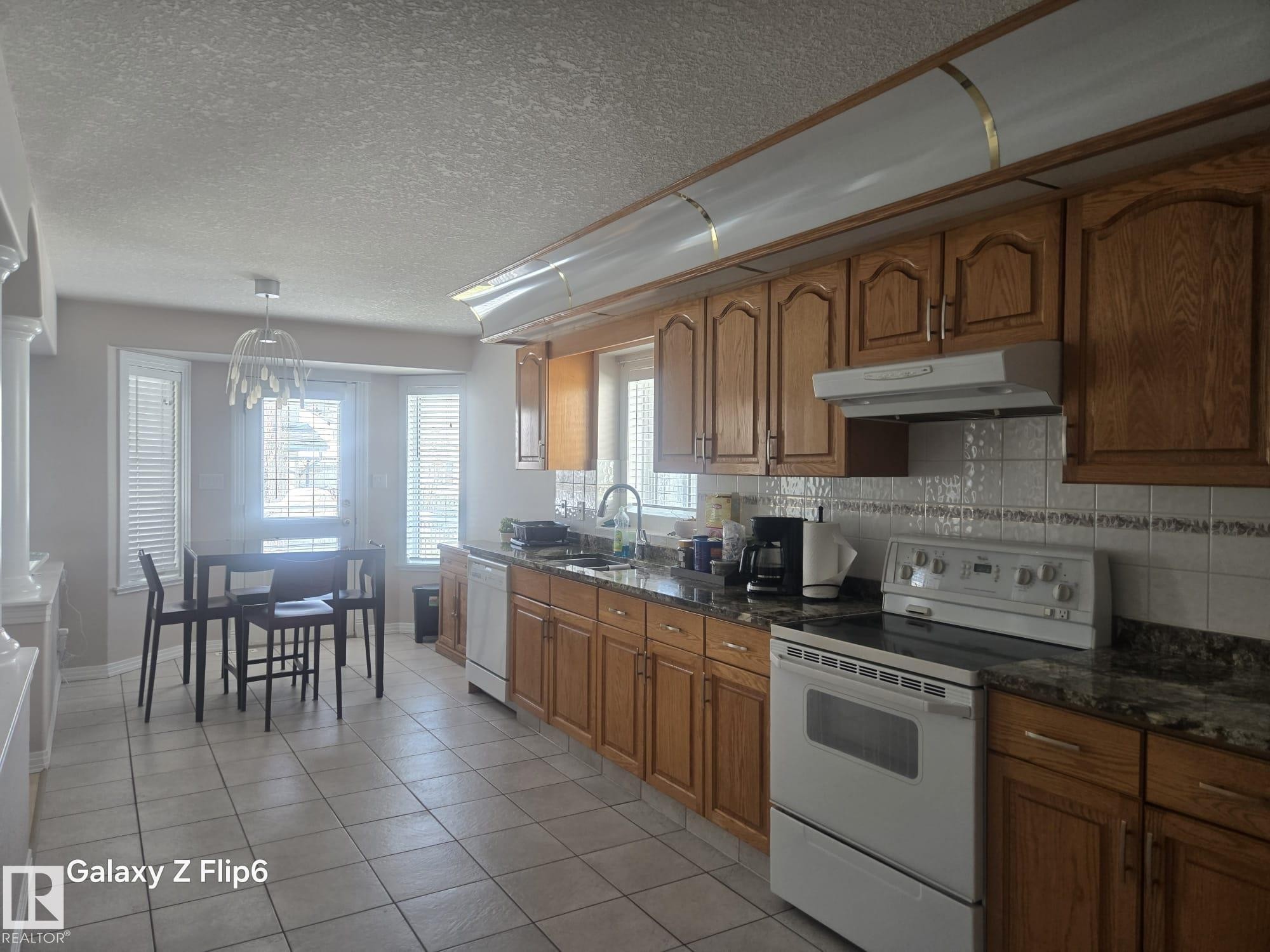 The kitchen features wood cabinetry, granite countertops, a tiled backsplash, and an electric range - Edmonton, AB - Indoor Photo Showing Kitchen