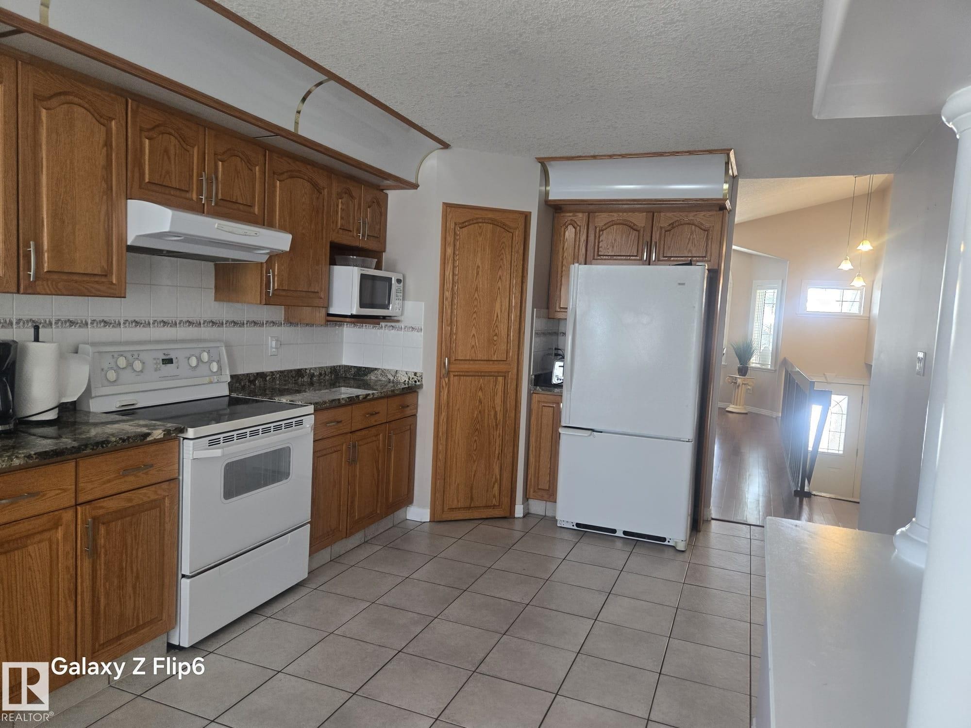 The kitchen features wood cabinetry, a white tile backsplash, and a white refrigerator and oven - Edmonton, AB - Indoor Photo Showing Kitchen