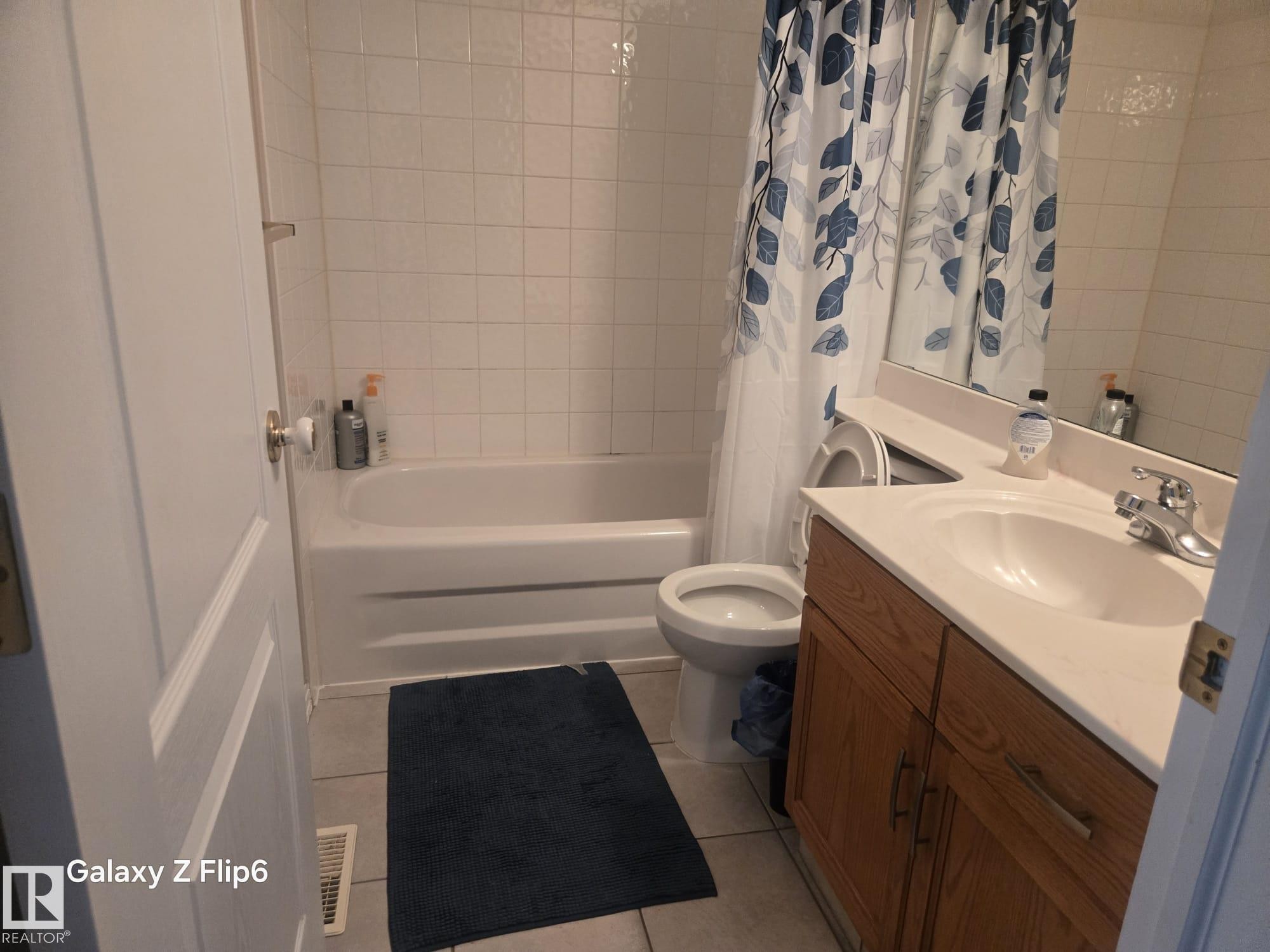 Bathroom with a vanity featuring a built-in sink, a bathtub with white tiled walls, and a toilet - Edmonton, AB - Indoor Photo Showing Bathroom