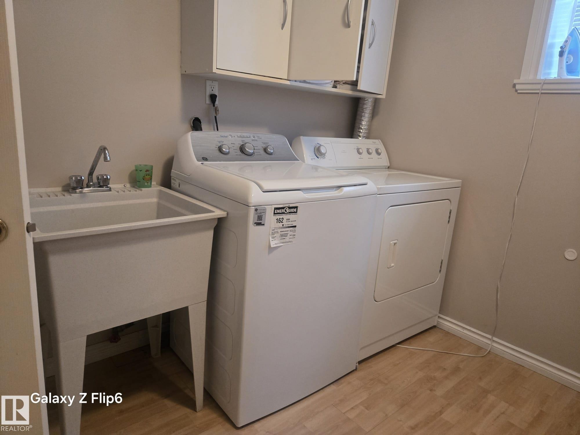 Dedicated laundry area featuring a utility sink, a white top-loading washing machine, and a white dryer - Edmonton, AB - Indoor Photo Showing Laundry Room