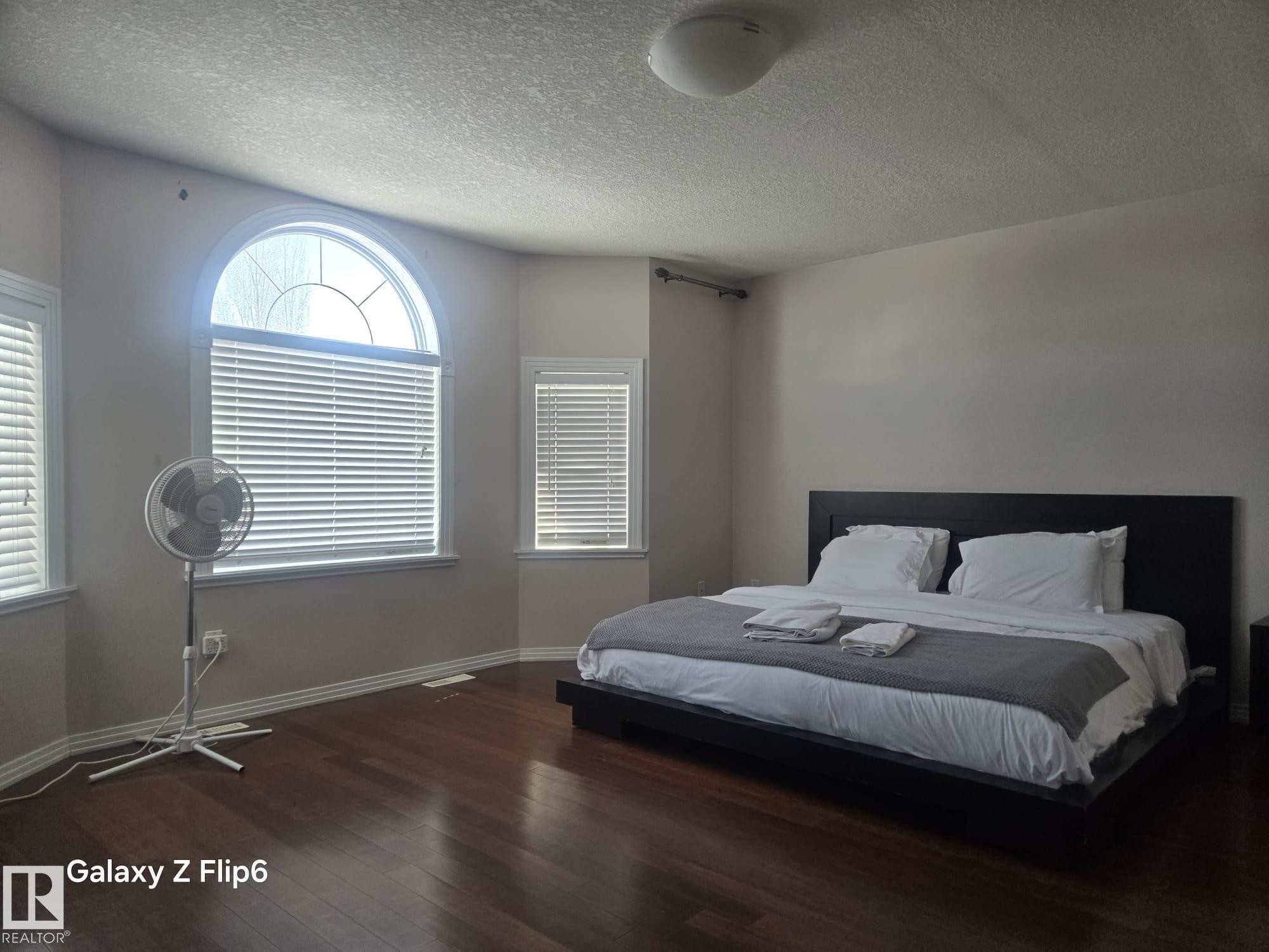 The property features hardwood floors throughout, with large windows providing natural light, including an arched window with blinds - Edmonton, AB - Indoor Photo Showing Bedroom