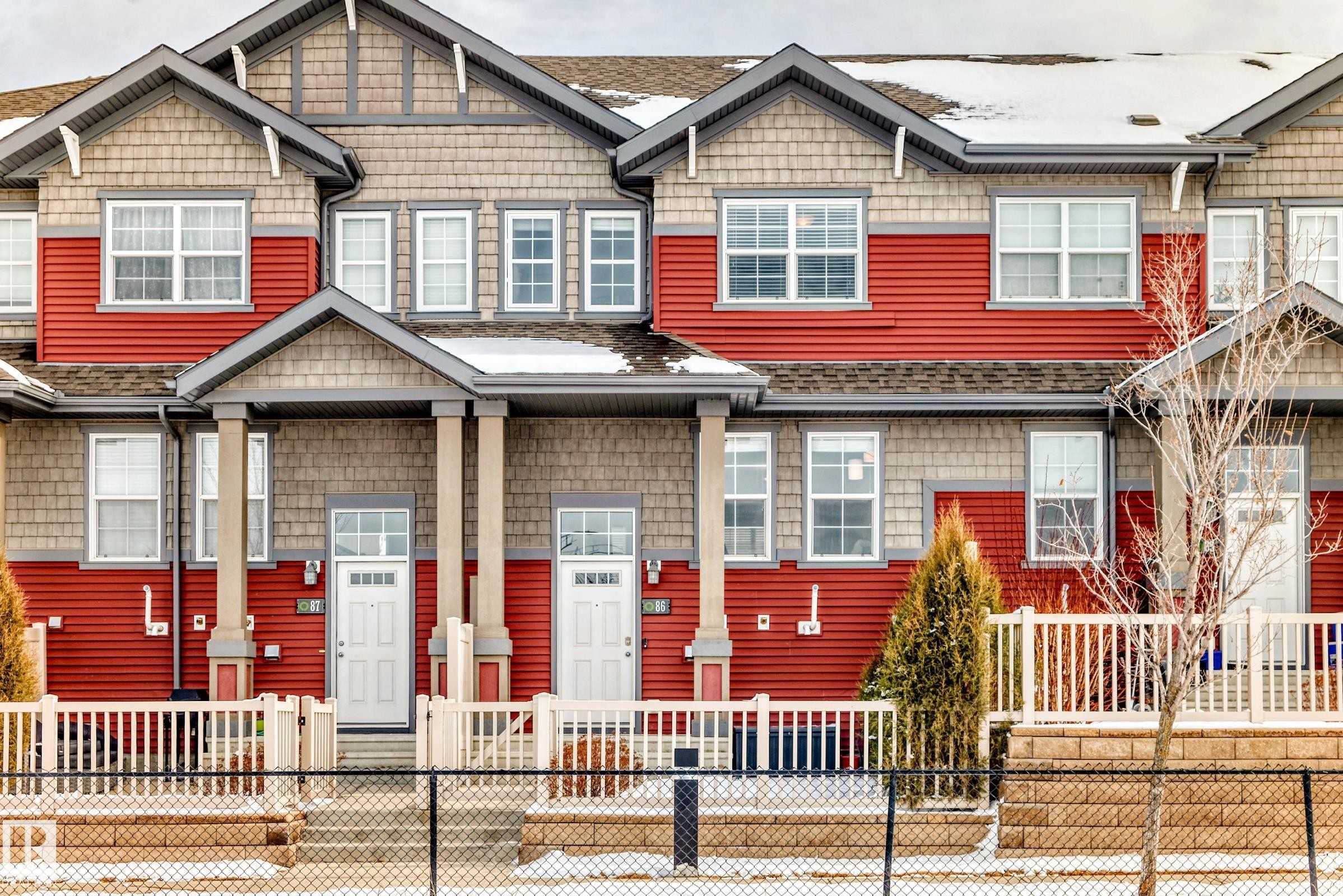 The property features a red and grey exterior with multiple windows and white doors - 86 4029 Orchards Drive, Edmonton, AB - Outdoor With Facade