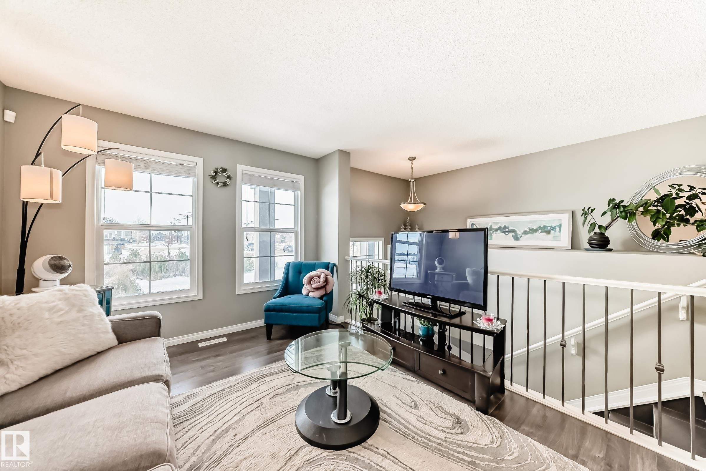 Living area featuring large windows, hardwood floors, and a railing overlooking a staircase - 86 4029 Orchards Drive, Edmonton, AB - Indoor Photo Showing Living Room
