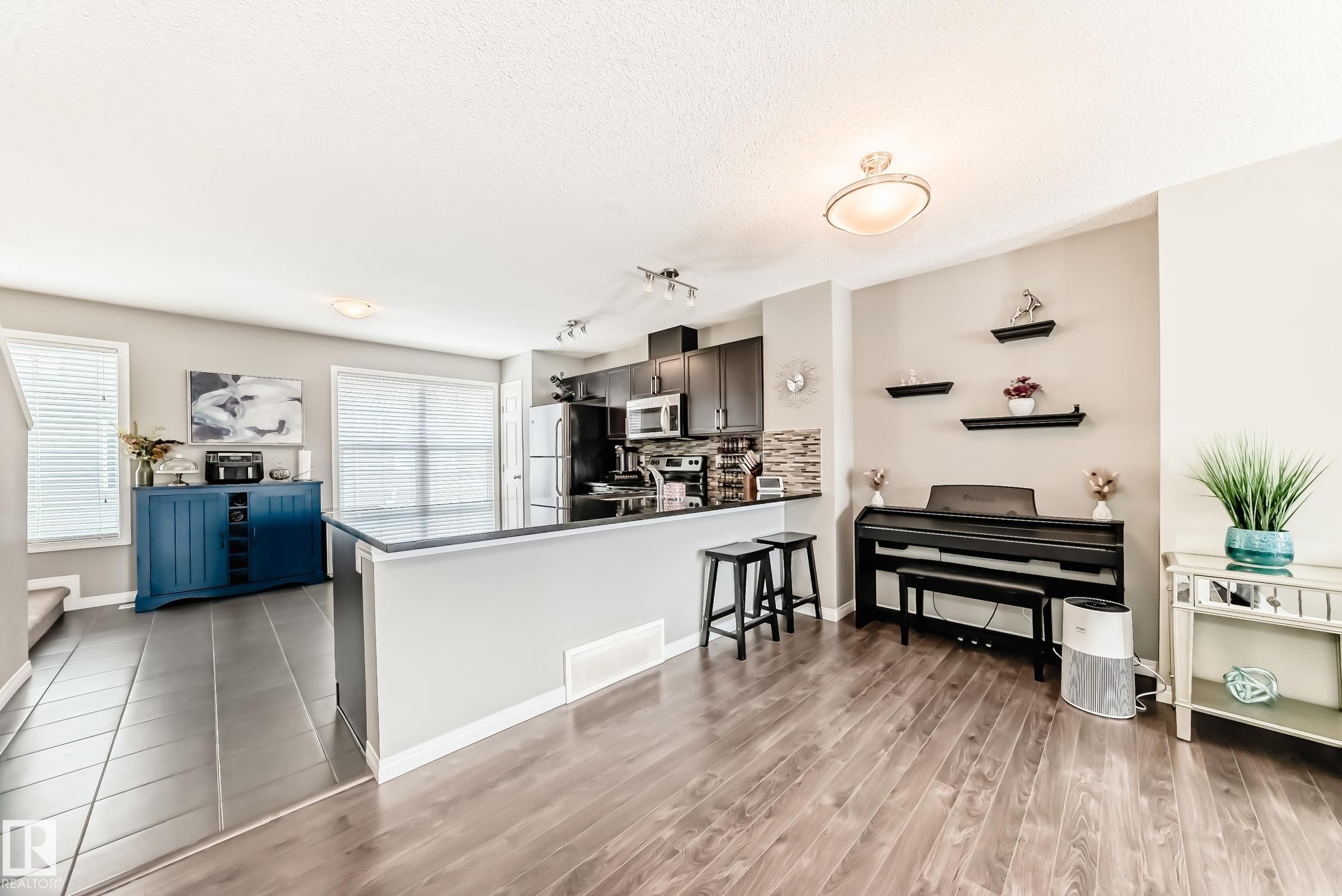 This bright interior features a kitchen with dark cabinetry, stainless steel appliances, and a tiled backsplash - 86 4029 Orchards Drive, Edmonton, AB - Indoor