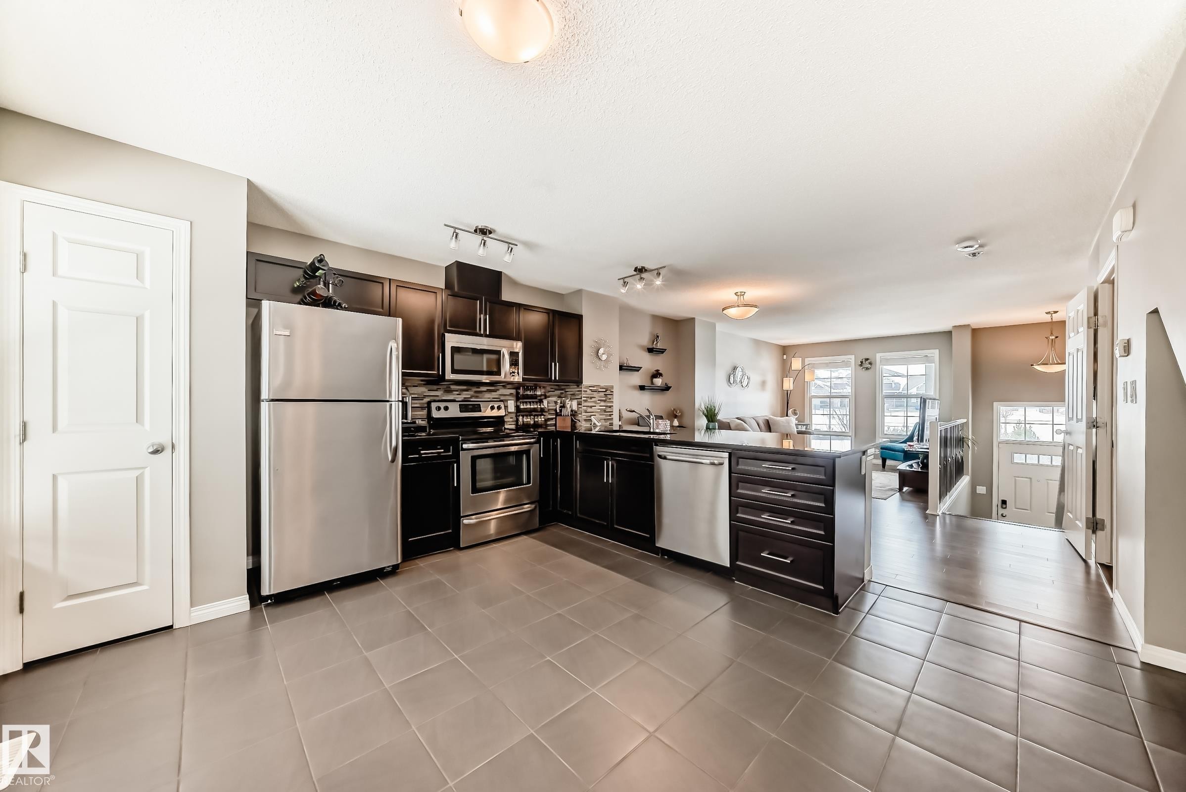 The kitchen features dark cabinetry, stainless steel appliances, and tiled flooring - 86 4029 Orchards Drive, Edmonton, AB - Indoor Photo Showing Kitchen