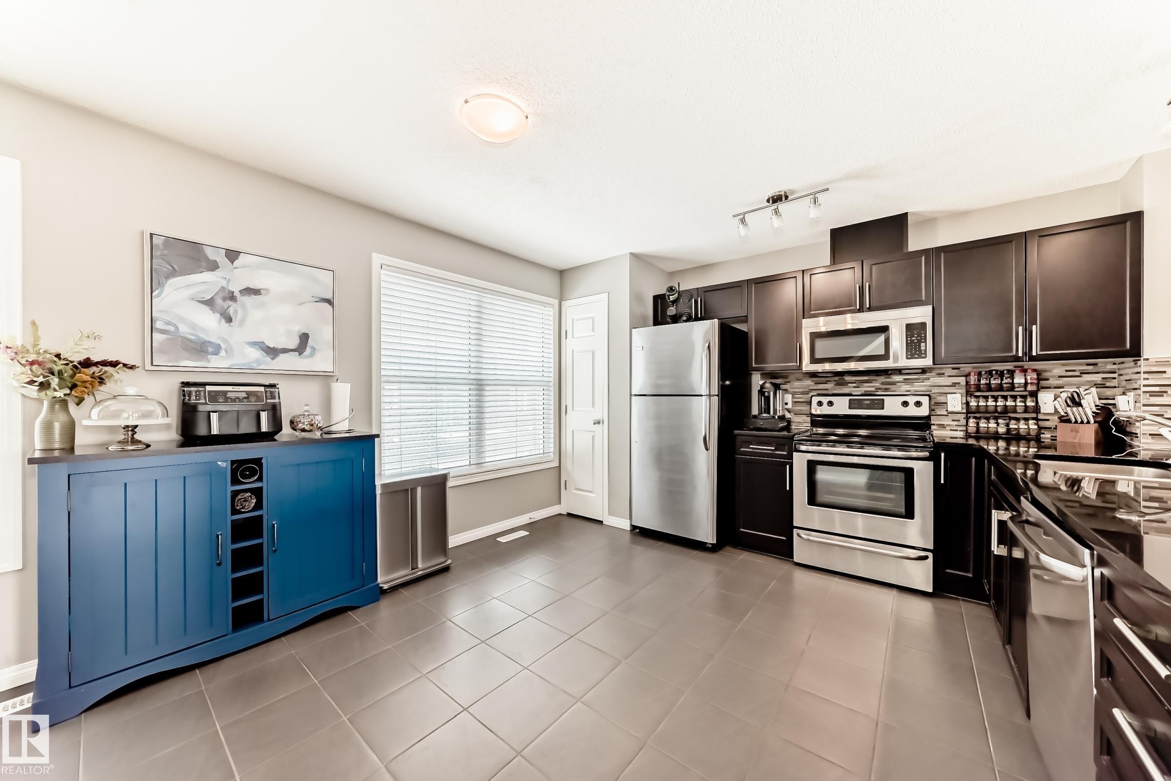 The kitchen features dark wood cabinetry, stainless steel appliances, and a tiled backsplash - 86 4029 Orchards Drive, Edmonton, AB - Indoor Photo Showing Kitchen With Upgraded Kitchen
