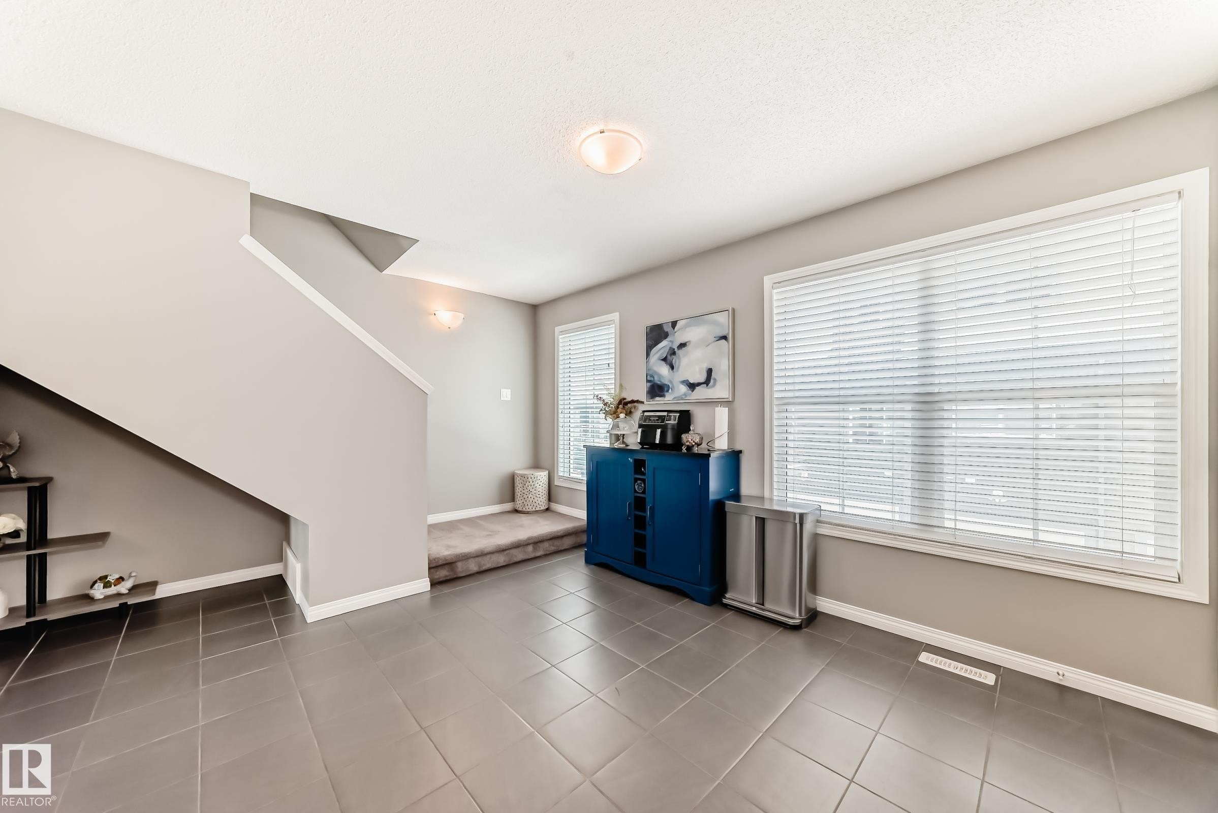 The foyer features tiled flooring, a prominent staircase, and large windows with blinds - 86 4029 Orchards Drive, Edmonton, AB - Indoor