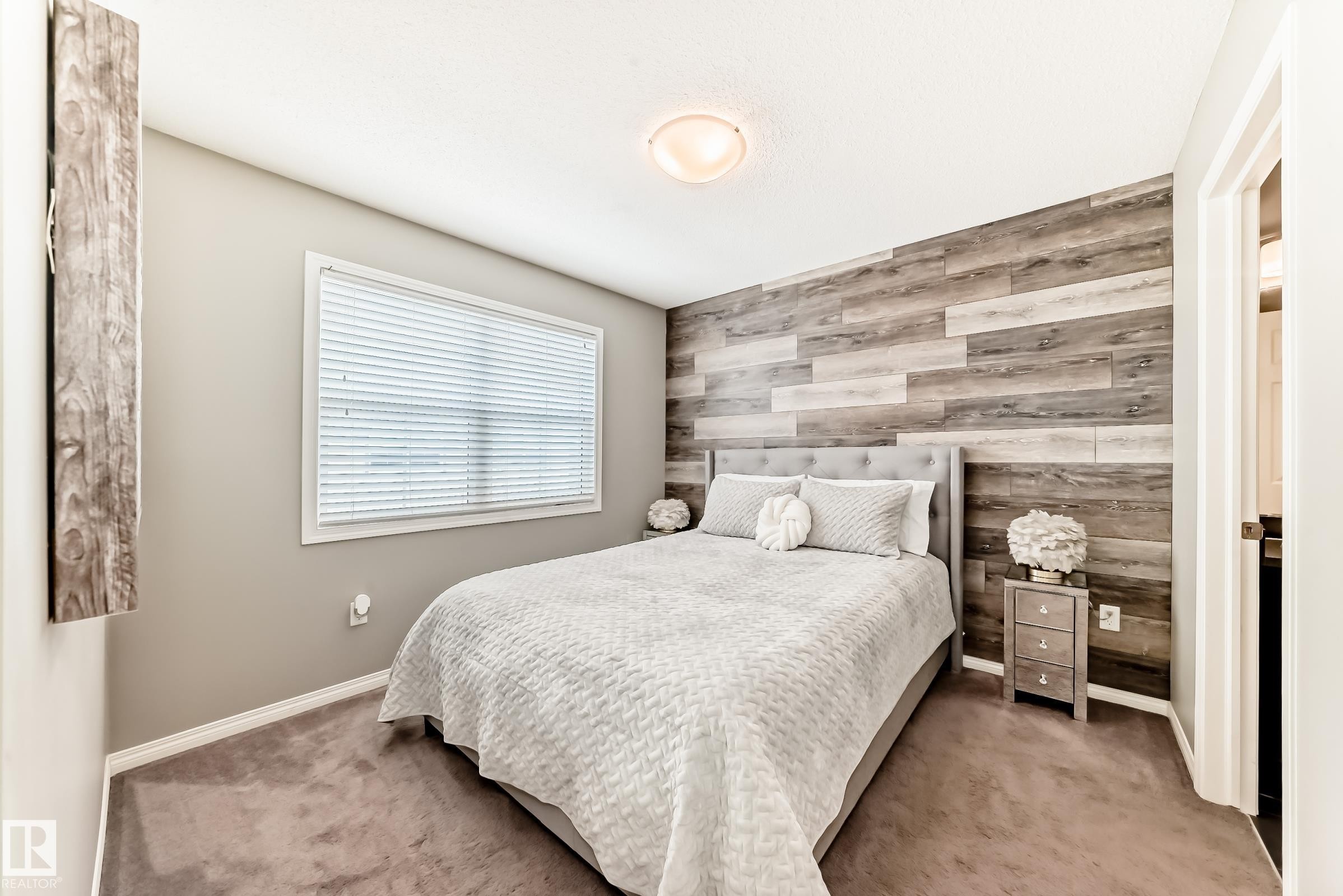 This room features a window with blinds, carpeted flooring, and a decorative wood panel accent wall - 86 4029 Orchards Drive, Edmonton, AB - Indoor Photo Showing Bedroom