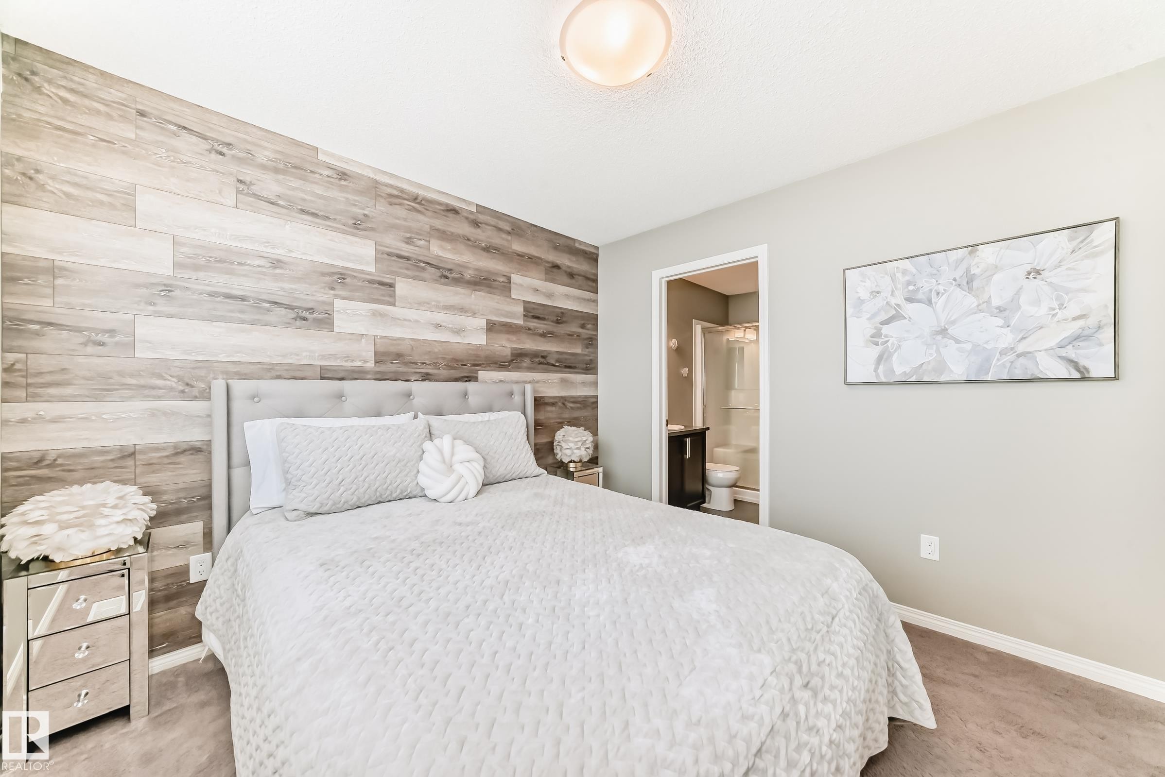 This bedroom features an accent wall with a wood plank design, light gray painted walls, and dark carpeting - 86 4029 Orchards Drive, Edmonton, AB - Indoor Photo Showing Bedroom