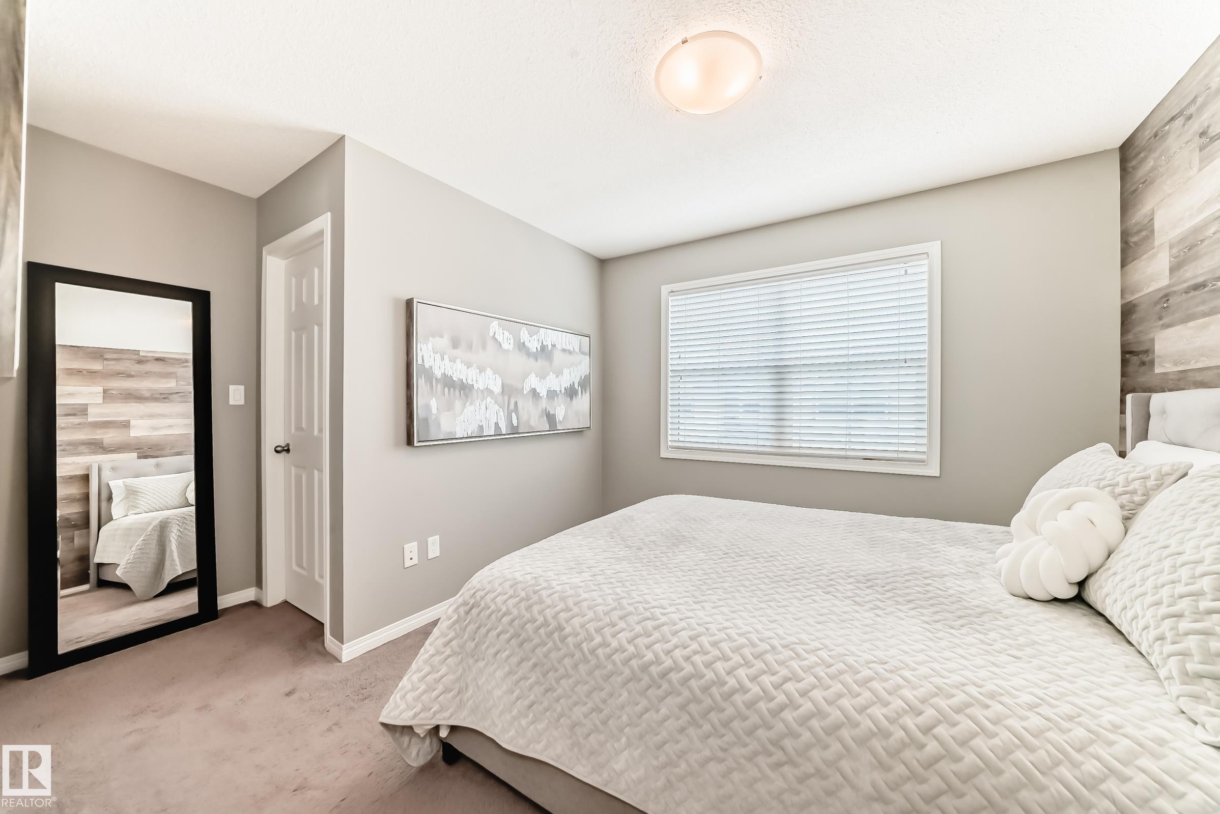 The room features light gray walls, a window with blinds, and a textured accent wall - 86 4029 Orchards Drive, Edmonton, AB - Indoor Photo Showing Bedroom