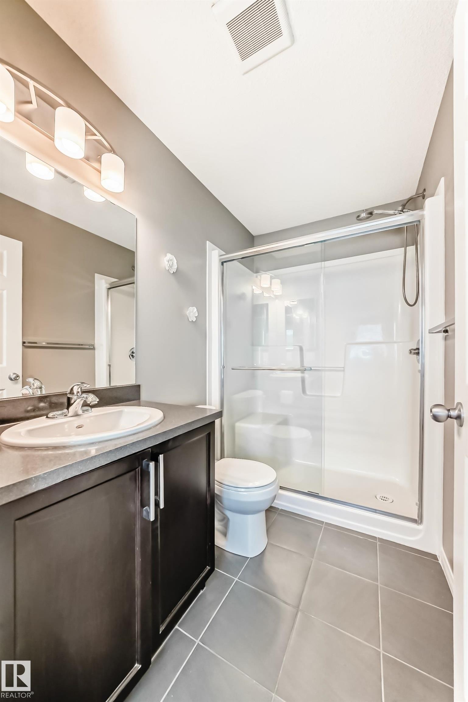 Bathroom featuring a dark wood vanity with a white basin sink, a mirrored wall, and a shower with a glass enclosure - 86 4029 Orchards Drive, Edmonton, AB - Indoor Photo Showing Bathroom